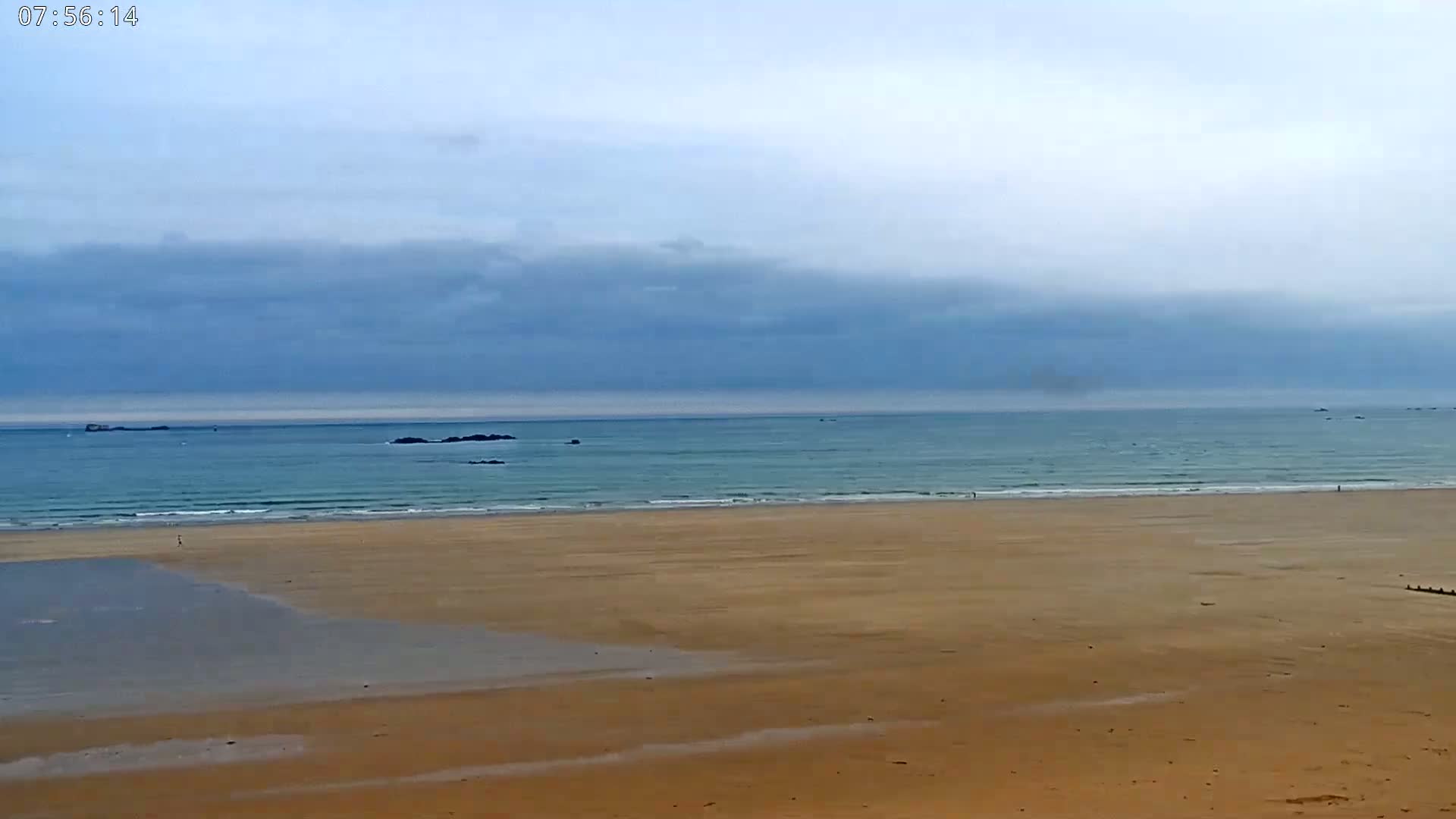 A wide sandy beach stretches to a calm, light teal ocean under a mostly cloudy sky.