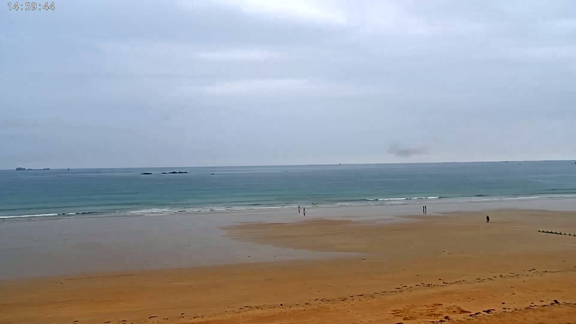 A wide sandy beach stretches to a calm, light-blue ocean under an overcast sky.