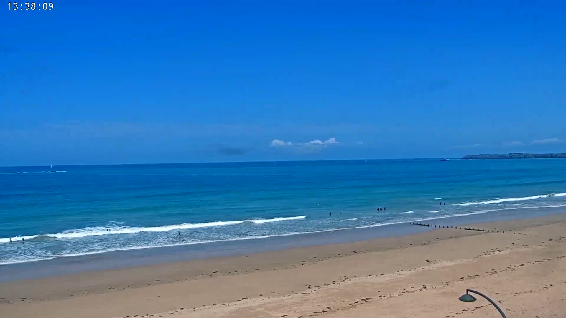 A sandy beach stretches to a calm, blue ocean under a clear, blue sky with a few small clouds.