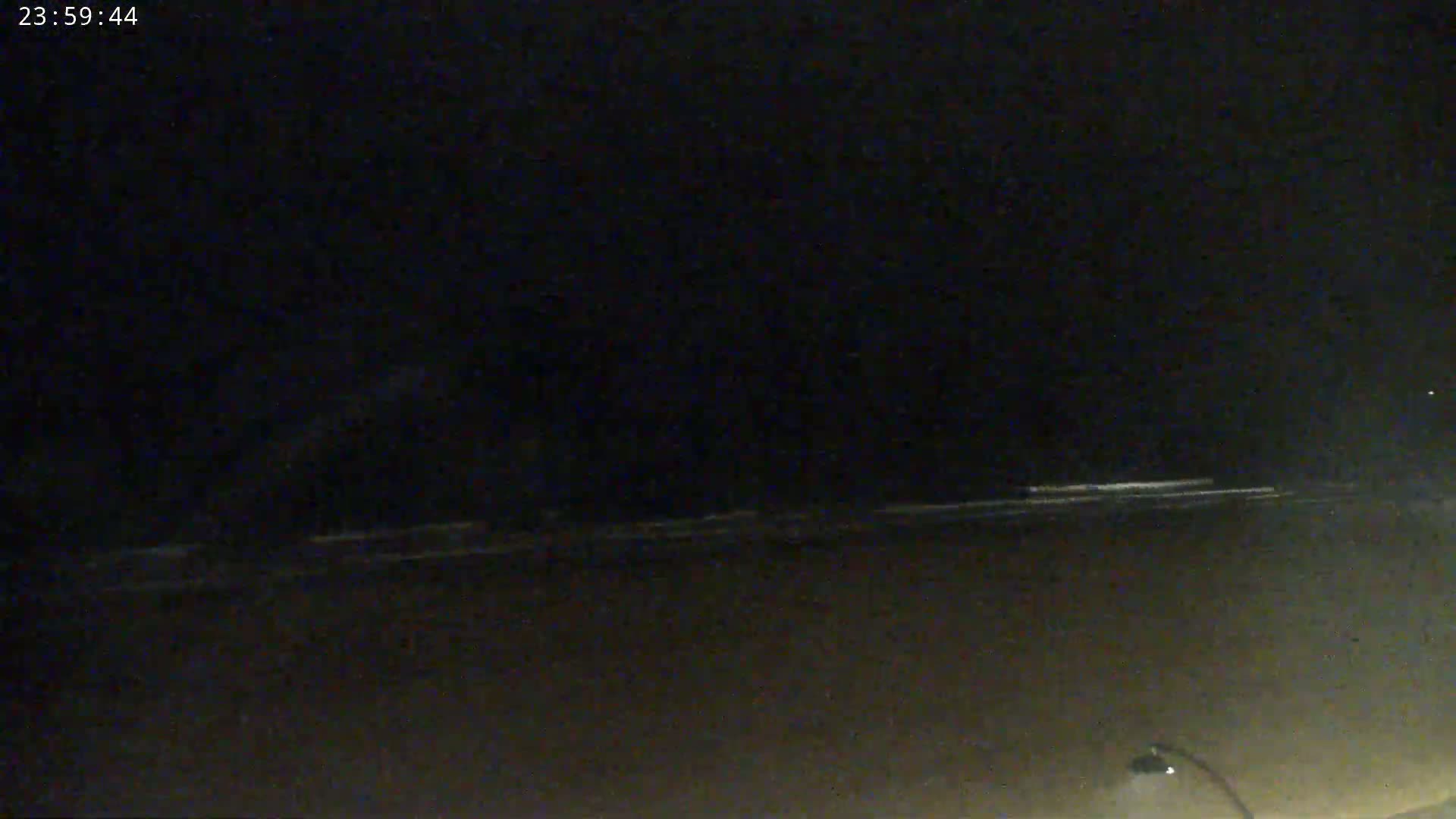 A dark, nighttime beach scene shows a dimly lit shoreline with small waves under a clear, black sky.