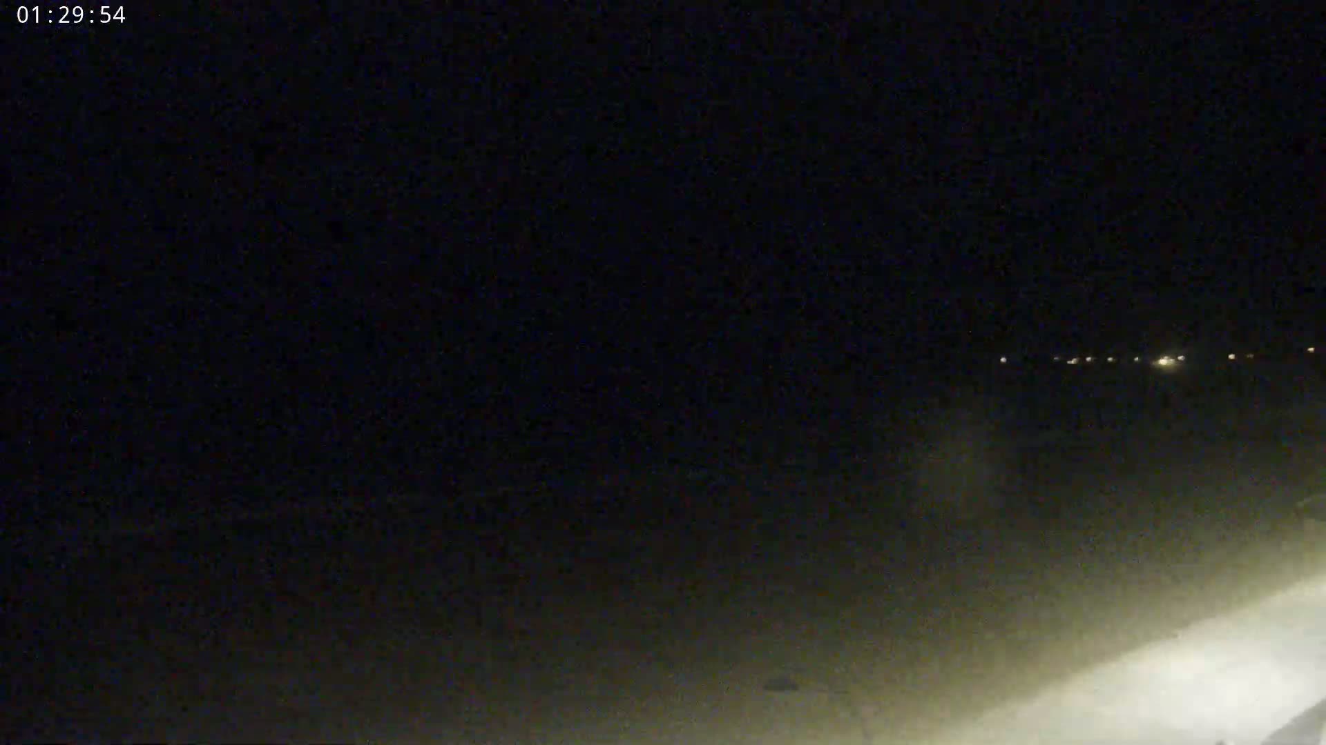 A nighttime, low-light outdoor scene shows a dark expanse with a faint line of distant lights on the horizon.