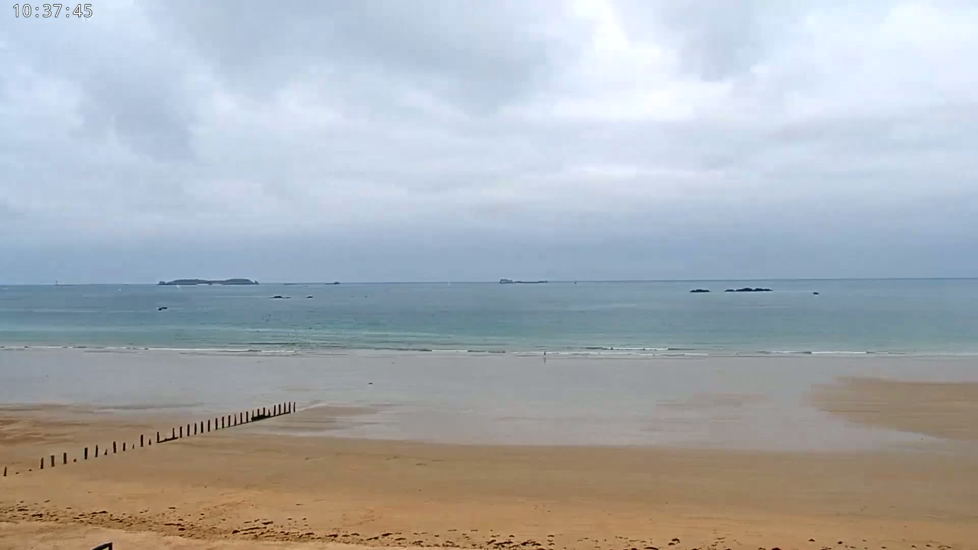 A sandy beach stretches to a calm, light-blue ocean under a cloudy sky.