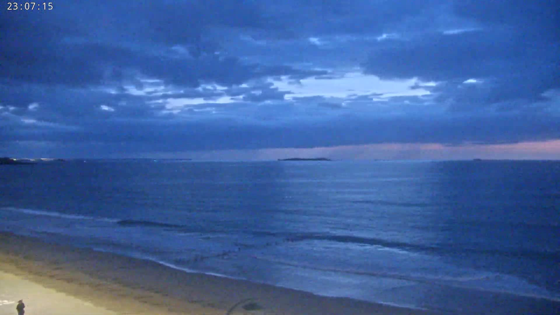A wide sandy beach stretches to a calm turquoise ocean under a mostly sunny sky with scattered clouds.