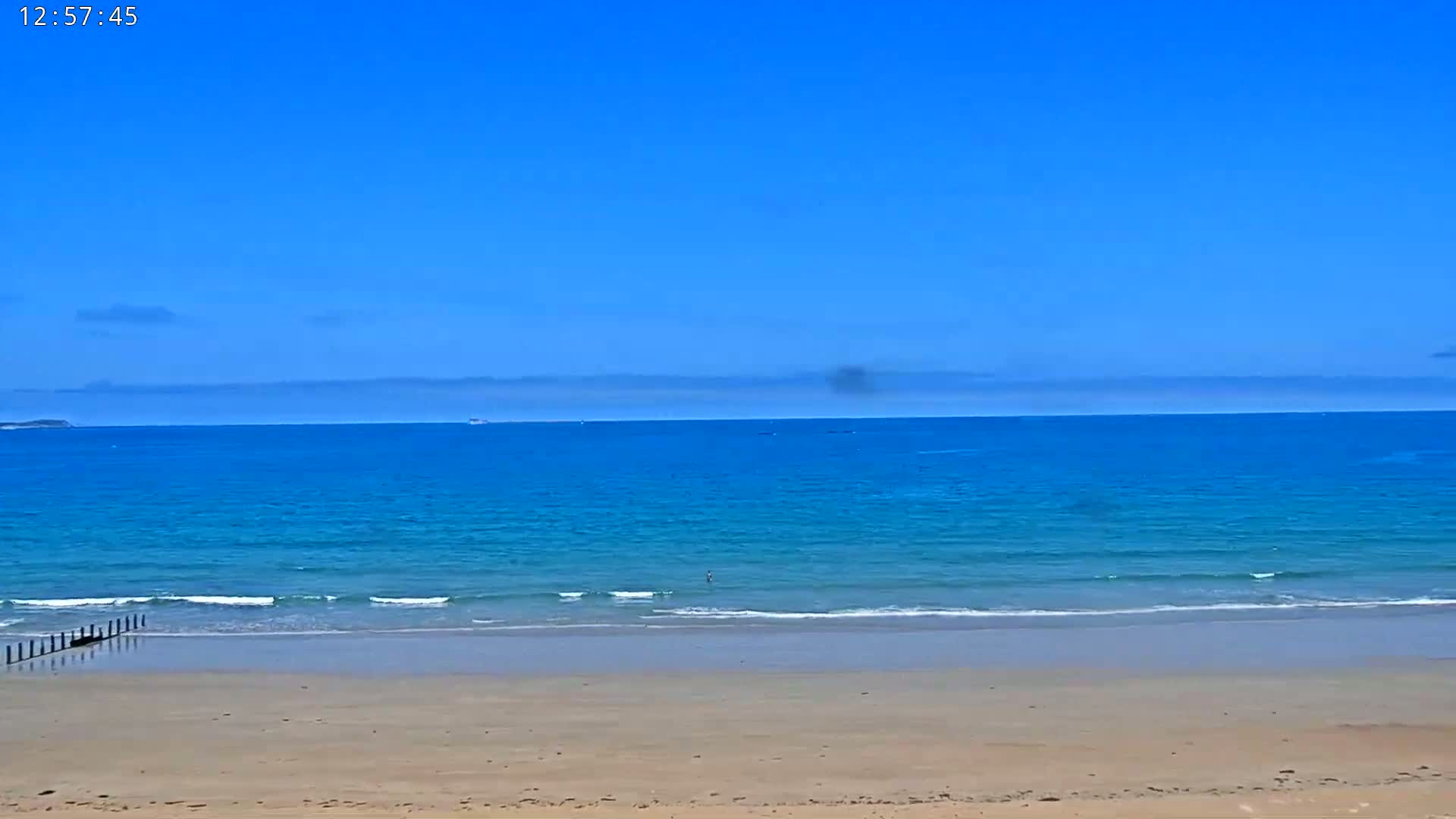 A sandy beach meets a calm, blue ocean under a clear, bright blue sky.