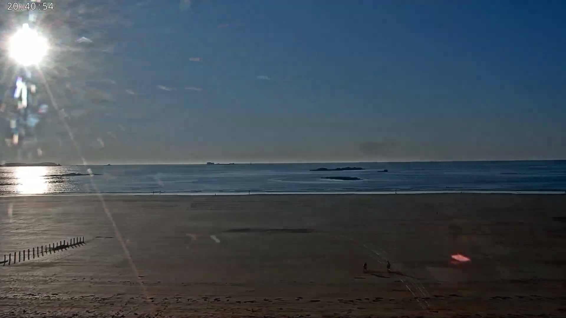A sandy beach stretches to a calm ocean under a bright, sunny sky.