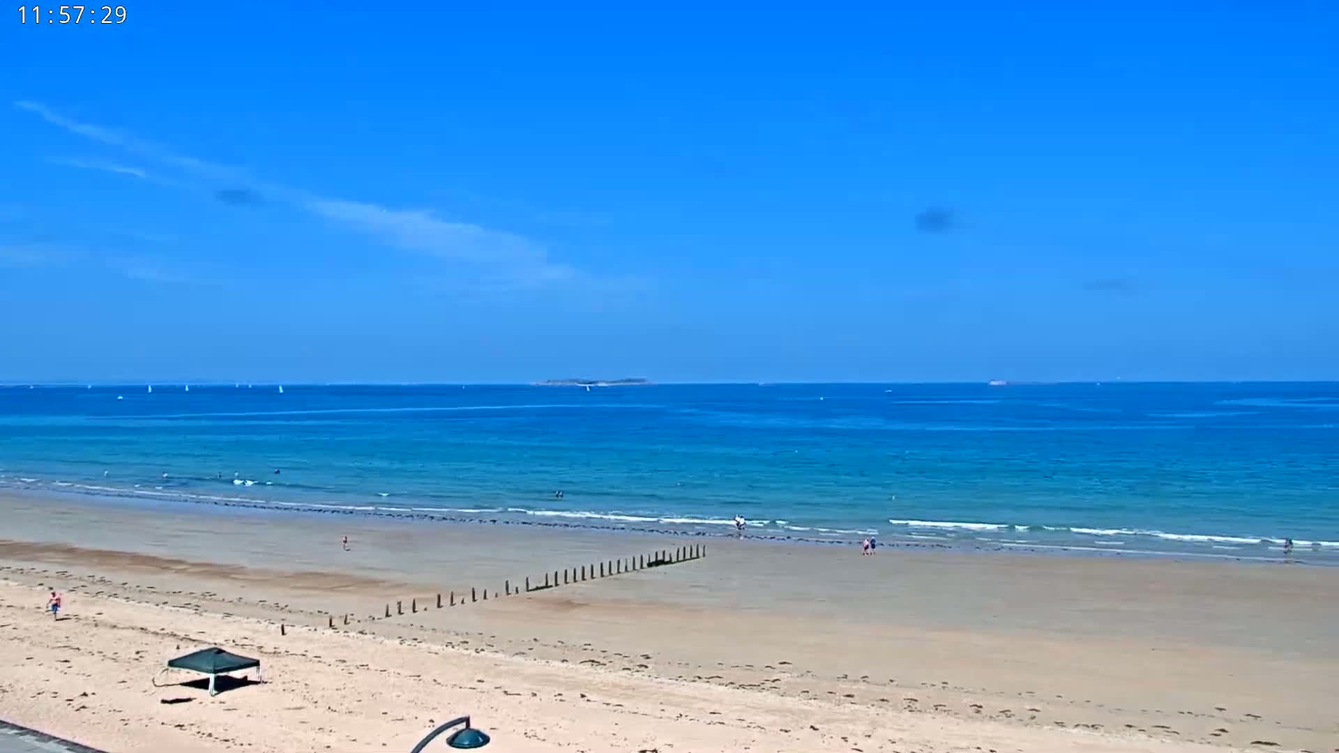 A sandy beach stretches to a calm, blue ocean under a clear, sunny sky.