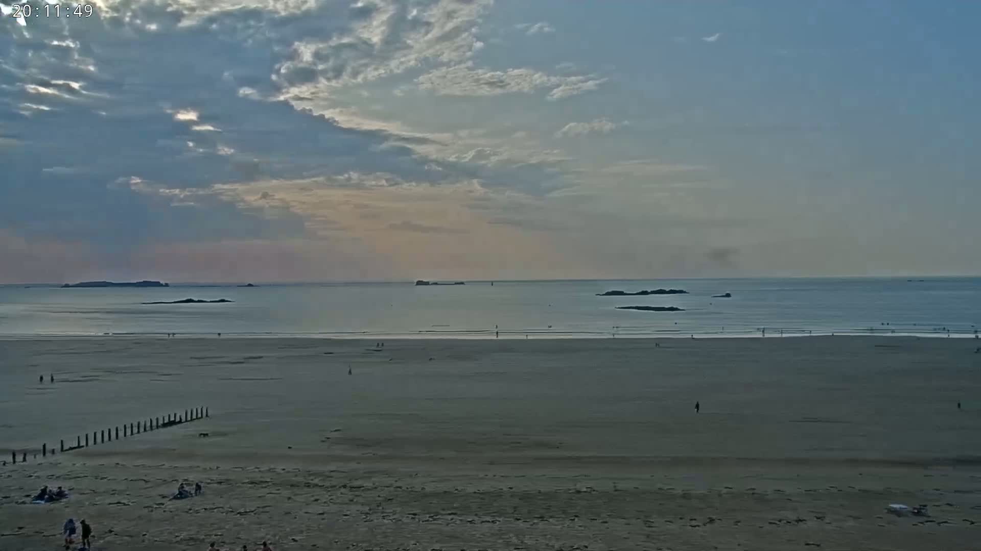 A wide sandy beach stretches to a calm ocean under a partly cloudy sky.