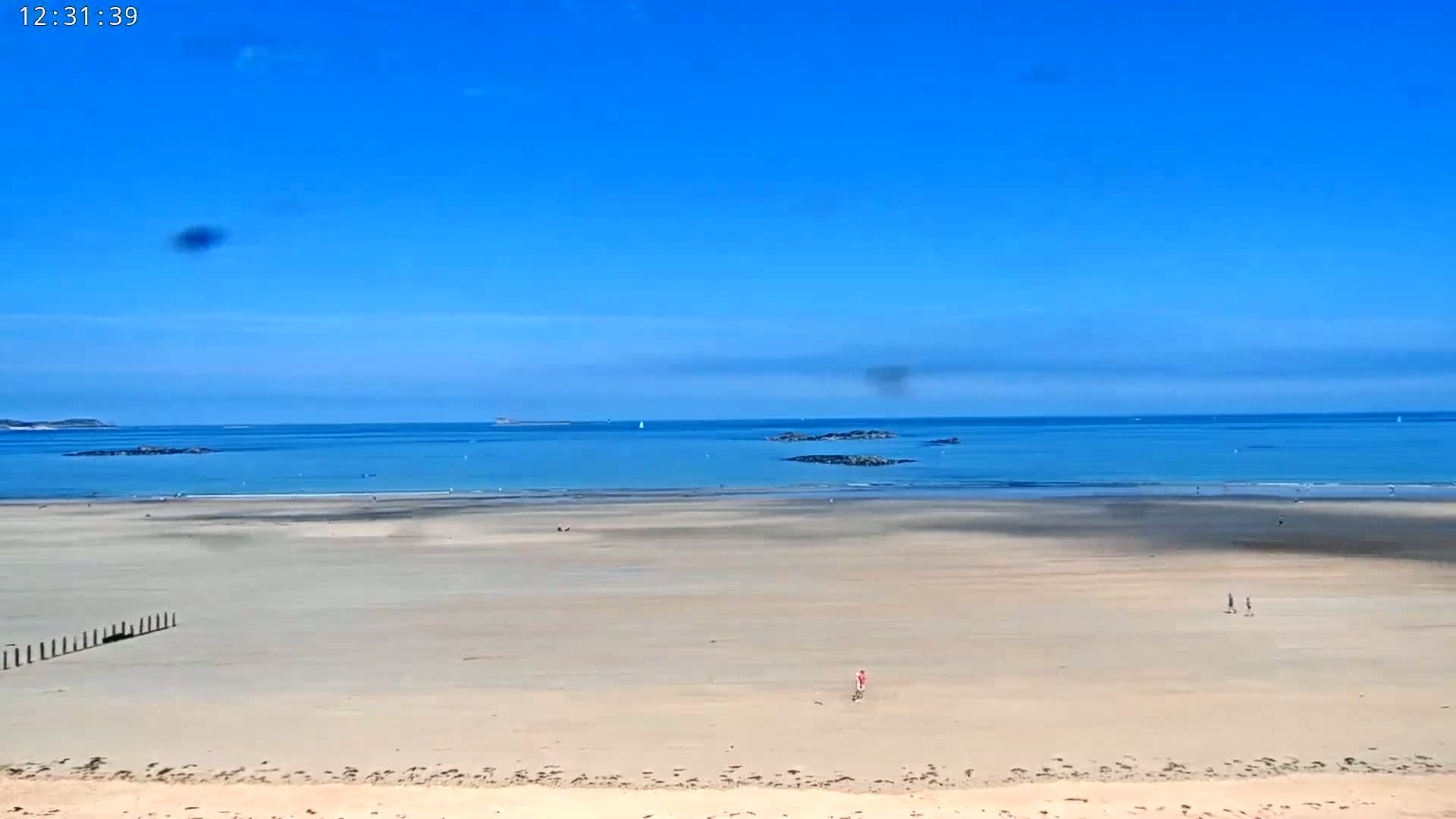 A wide, sandy beach stretches to a calm, light-blue ocean under a clear blue sky.