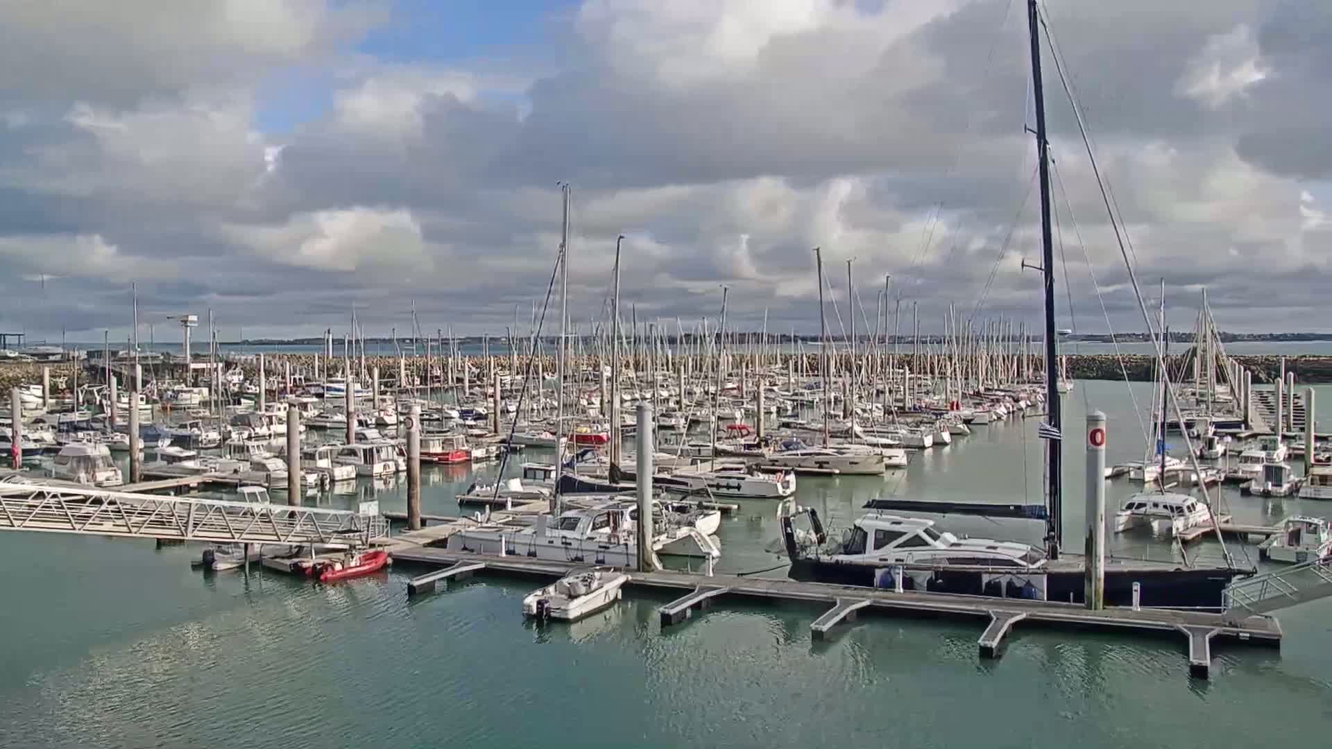 A large marina filled with numerous sailboats and motorboats under a partly cloudy sky.