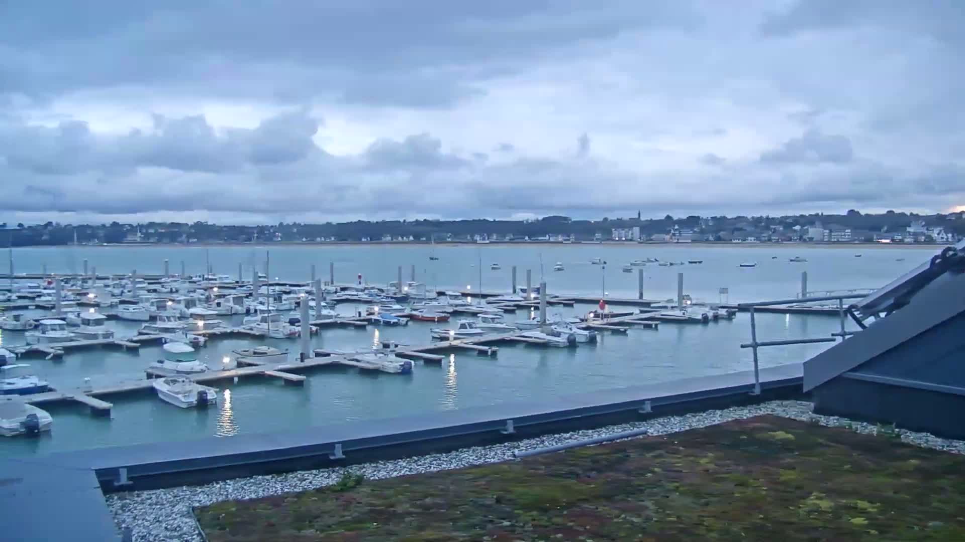 A marina filled with numerous boats is viewed from a rooftop under a cloudy sky.
