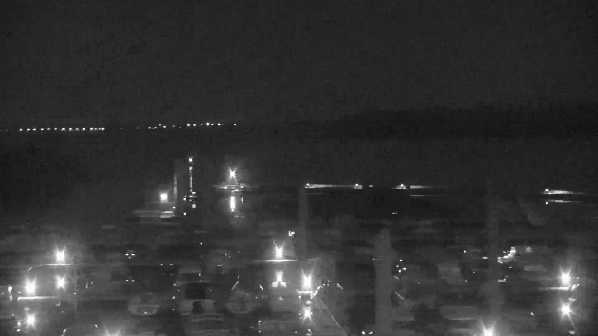 A nighttime, low-light view of a city or town near a body of water, showing numerous lights from vehicles and buildings.