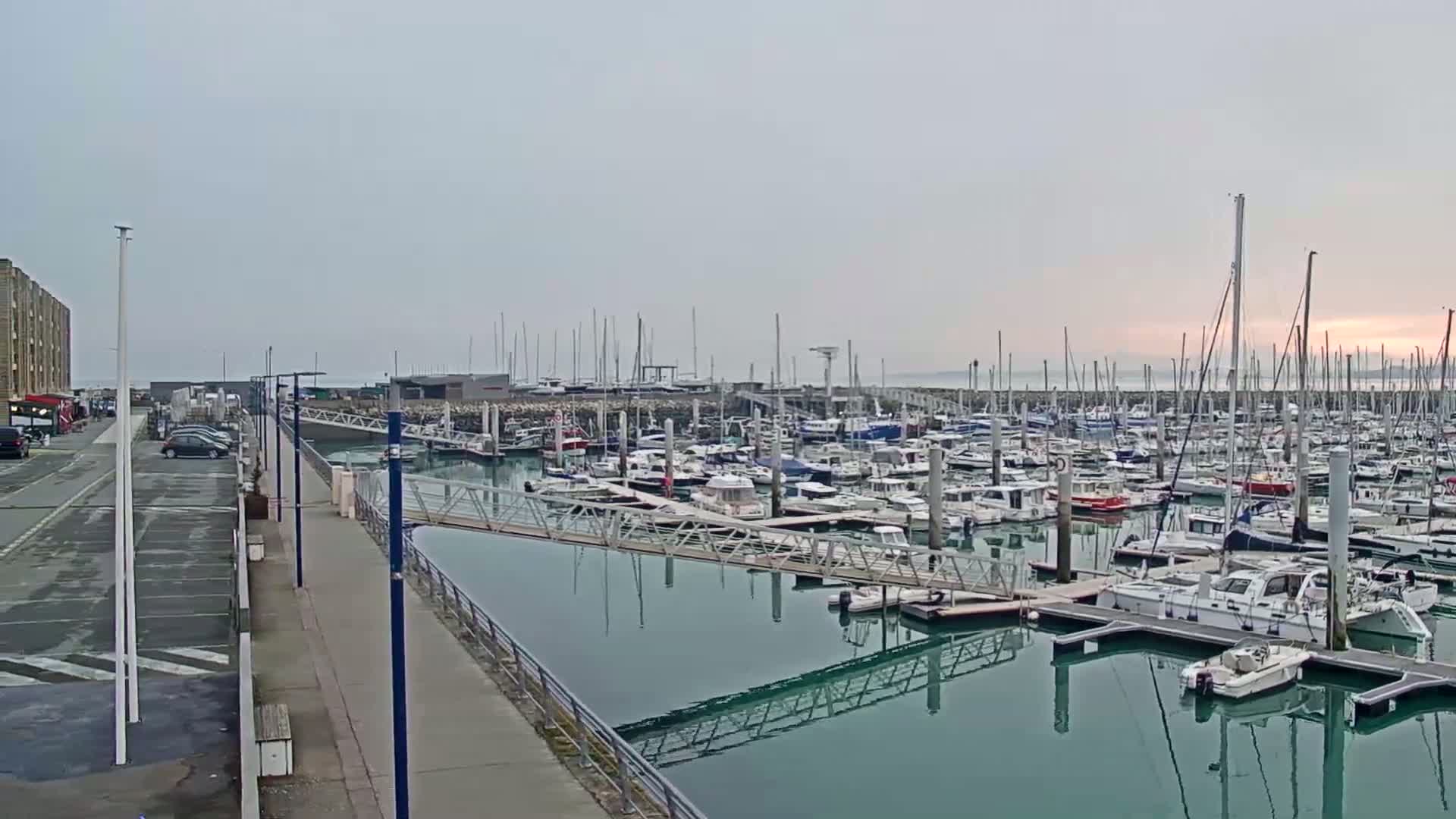 A marina filled with numerous boats and yachts is seen on a calm, overcast day.