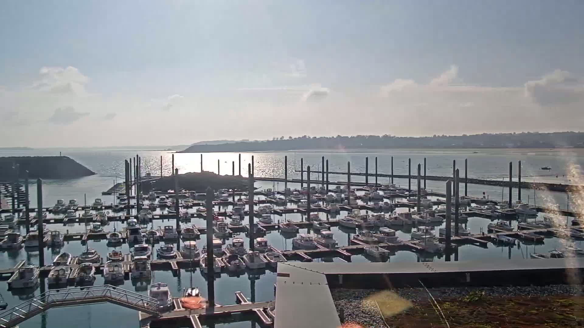 A marina filled with numerous boats is situated on calm water under a partly cloudy sky.