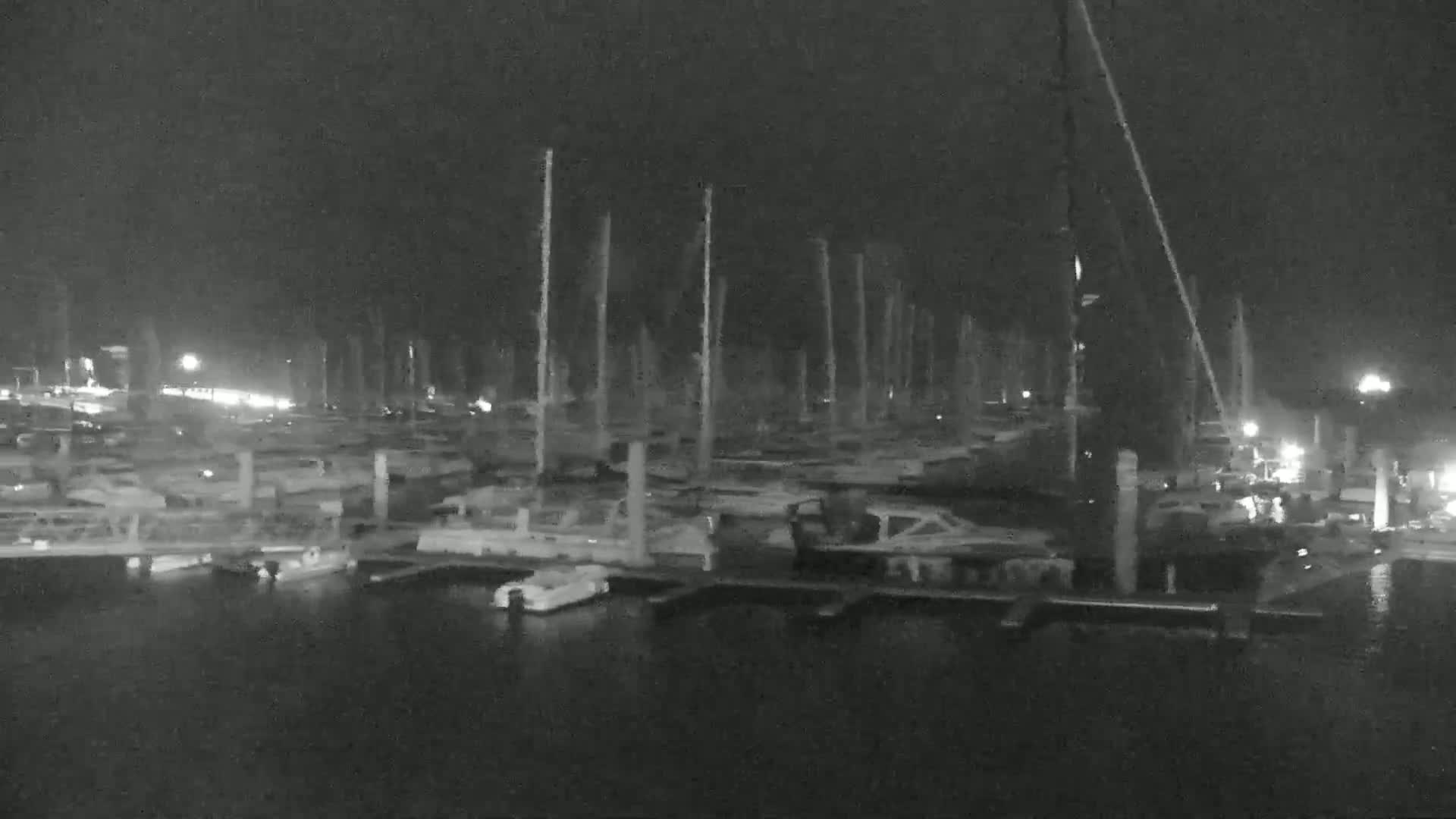 A nighttime, low-light image shows numerous boats docked at a marina.
