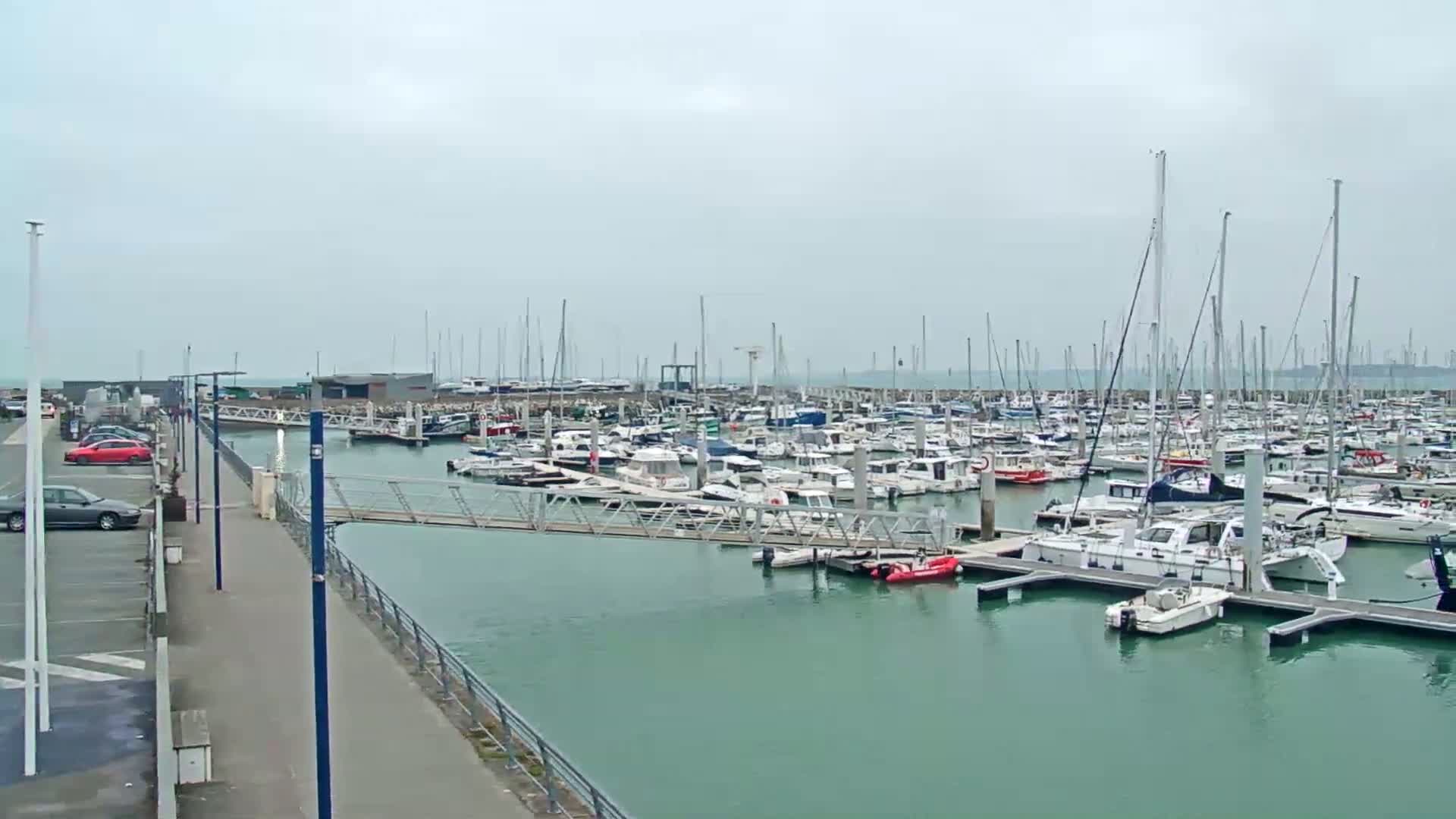 A marina filled with numerous sailboats and motorboats is seen on an overcast day.