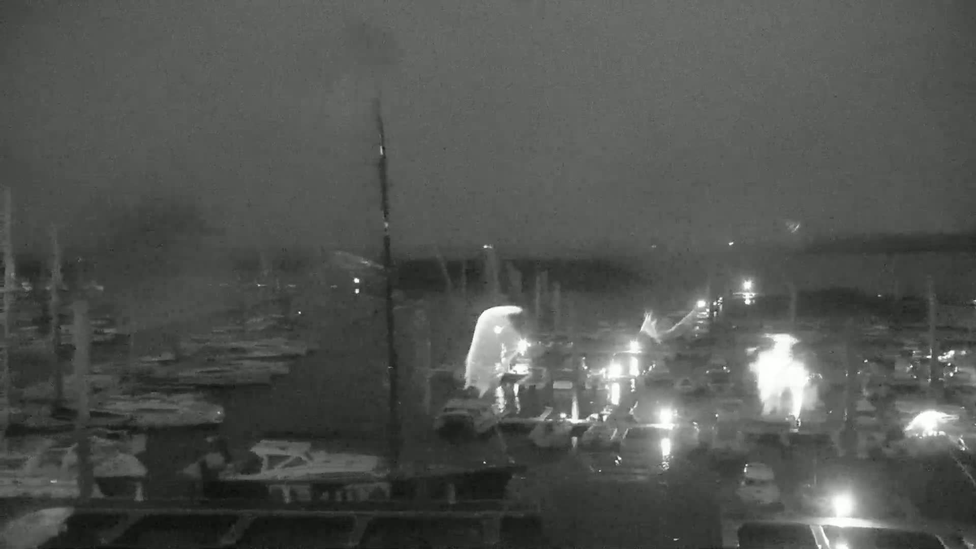 A nighttime, low-light view of a marina with many boats docked, under a dark, cloudy sky.