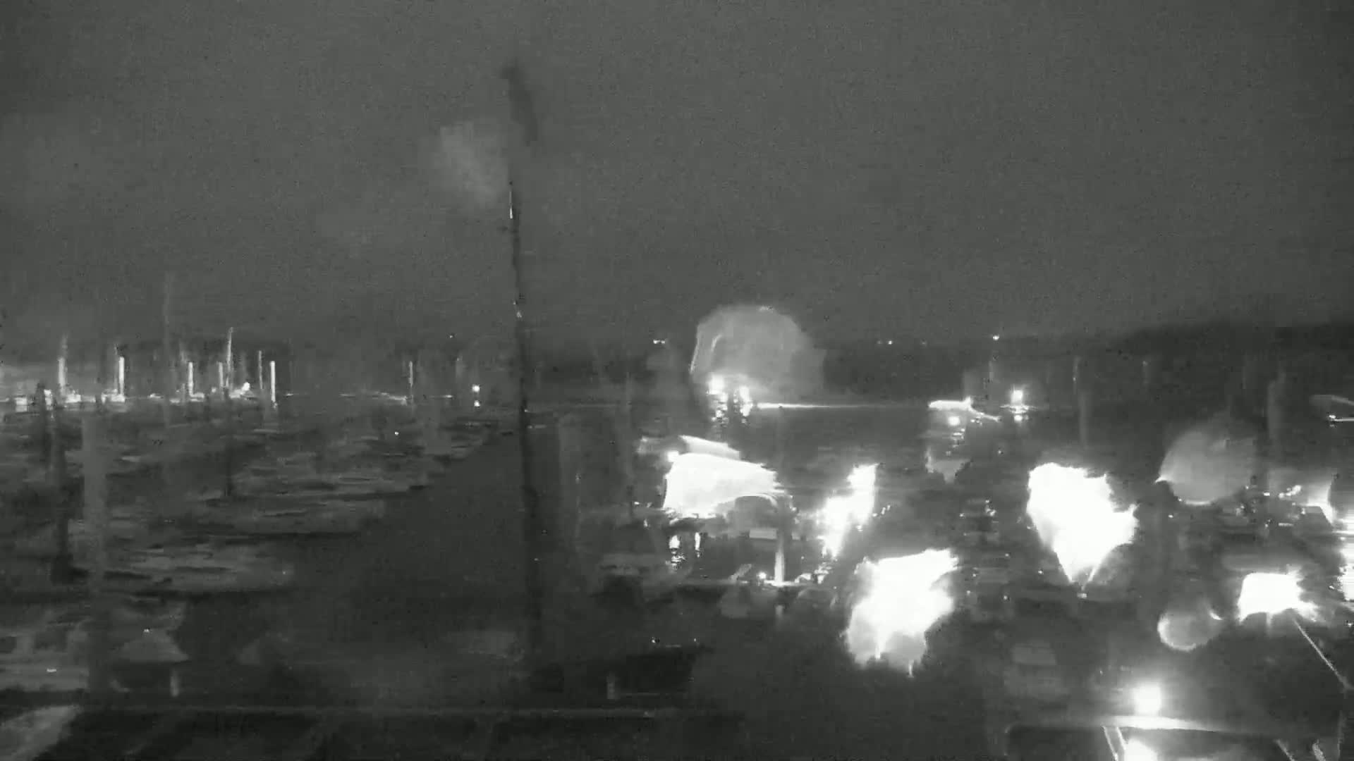 A nighttime, low-light view of a marina with many boats, some of which appear to have lights on, under a dark, possibly cloudy sky.