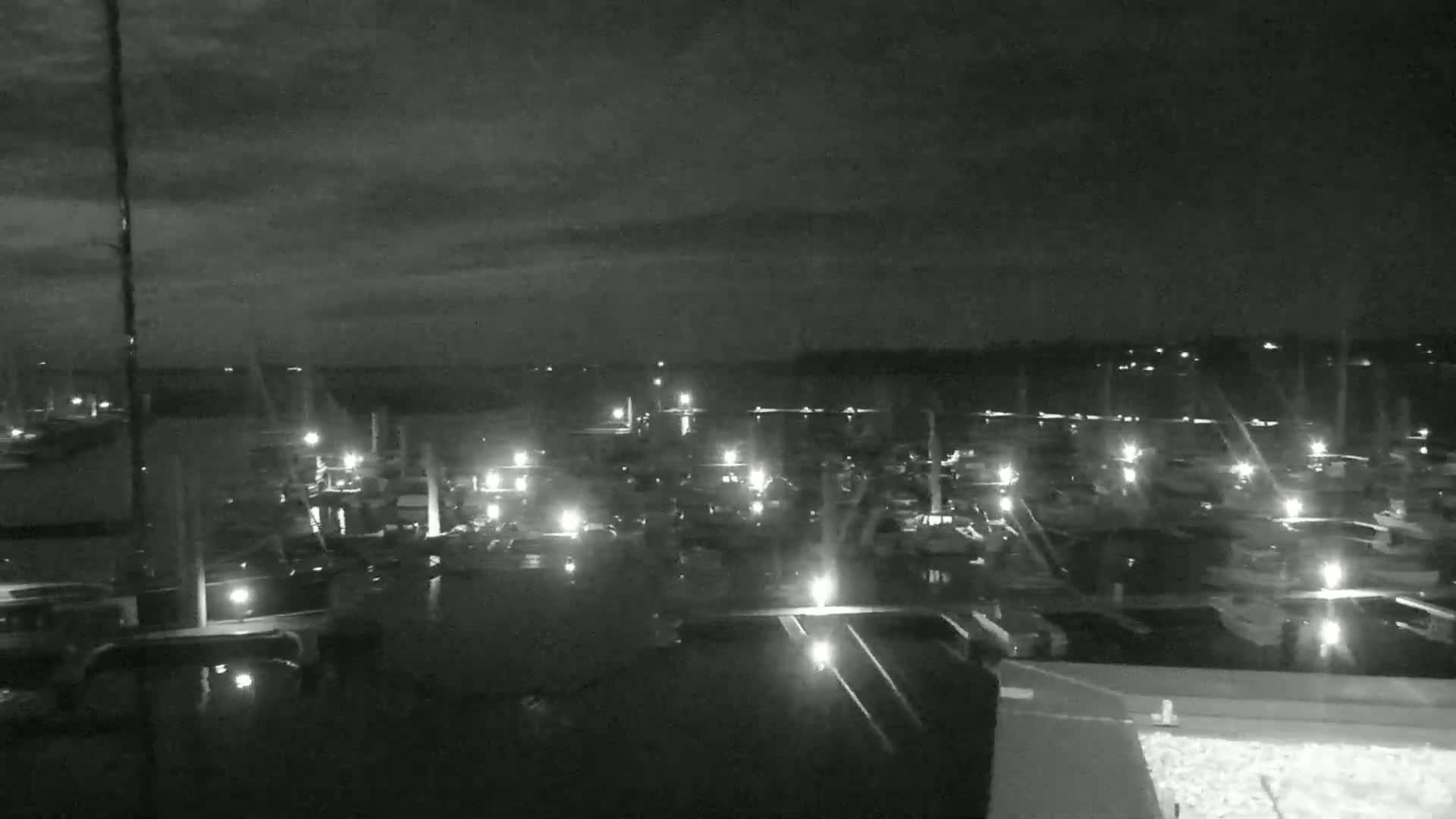 A nighttime, overcast view of a marina filled with numerous boats illuminated by their lights.