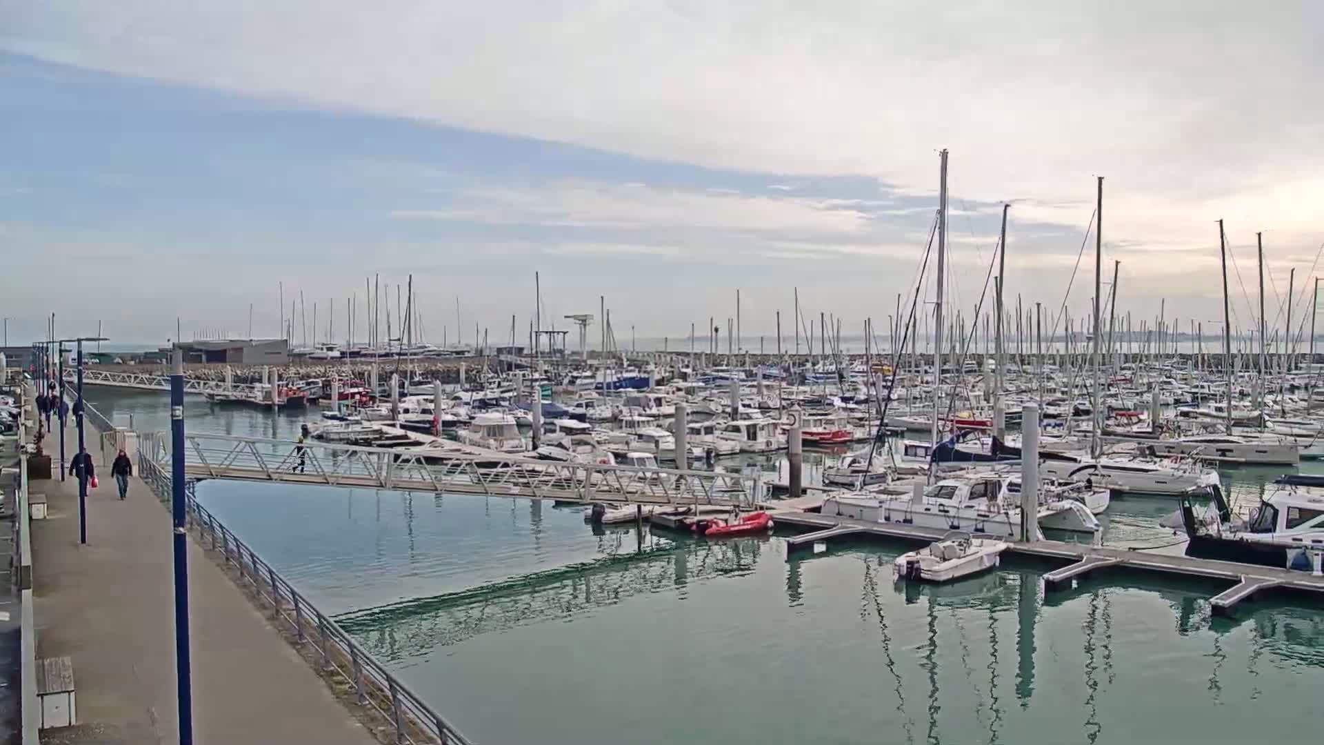 A marina filled with numerous sailboats and motorboats on a partly cloudy day.