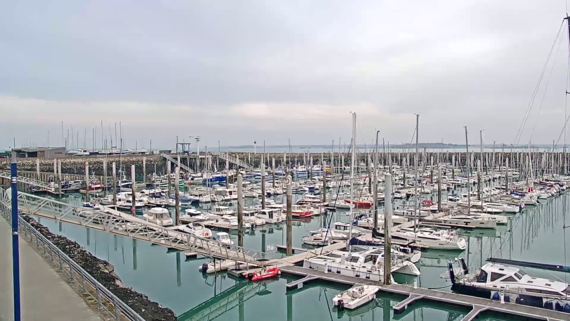 A marina filled with numerous sailboats and motorboats is seen on an overcast day.
