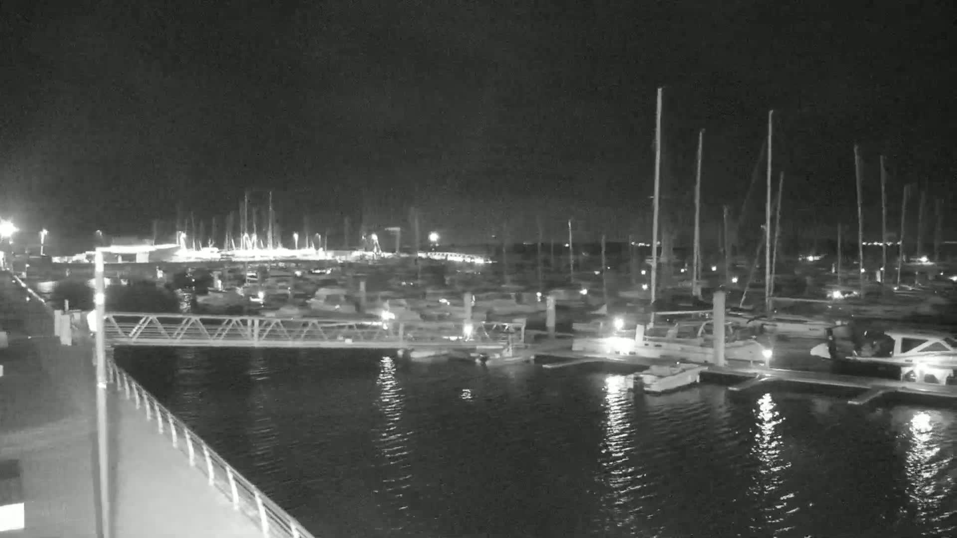 A nighttime view of a marina filled with docked boats and yachts under a dark sky.