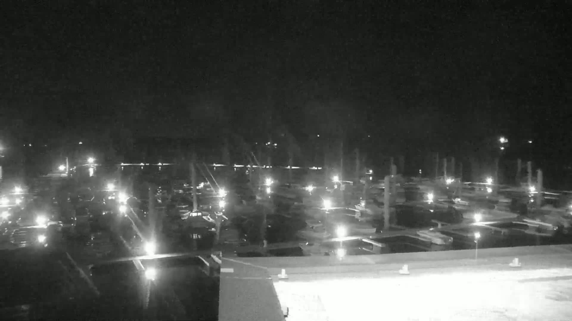 A nighttime, aerial view of a marina filled with numerous boats illuminated by lights.