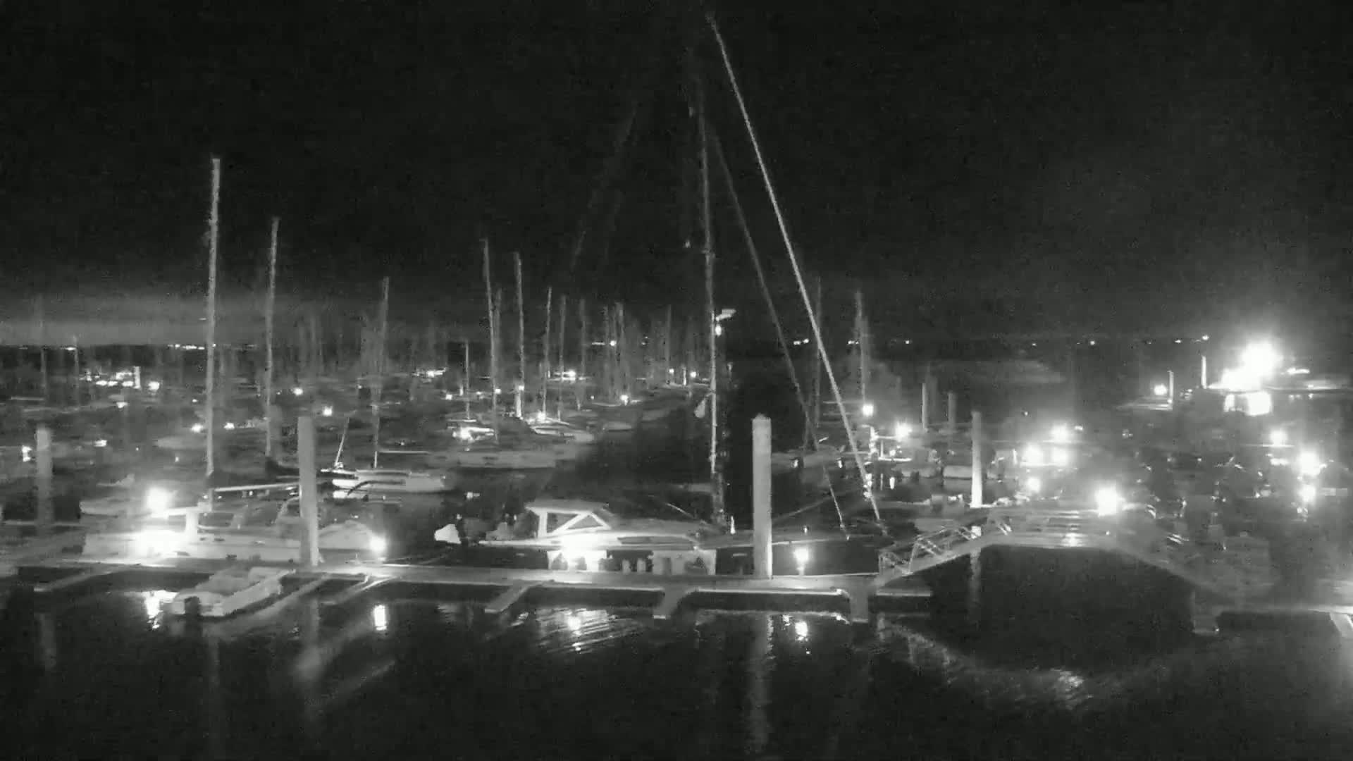A nighttime, low-light view of a marina filled with sailboats docked at their slips.