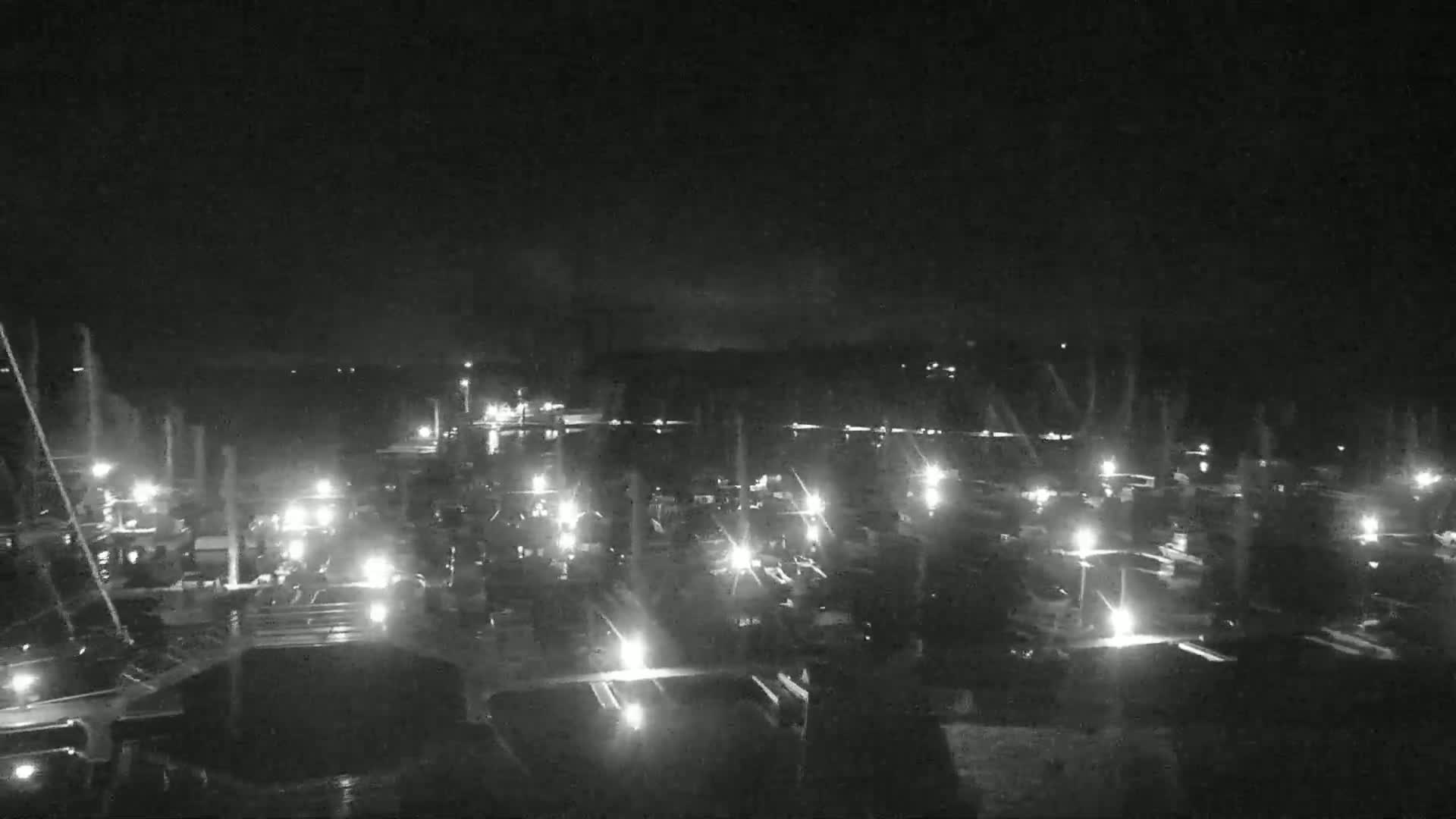 A nighttime, aerial view of a marina with numerous boats illuminated by their lights.