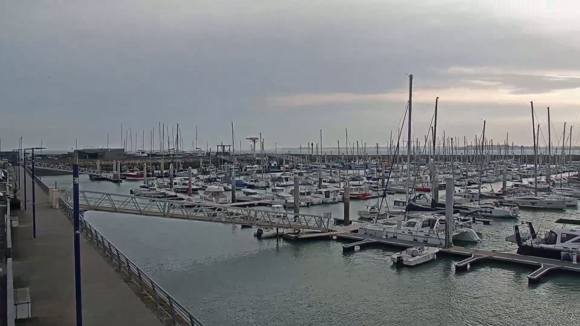 A marina filled with numerous sailboats and motorboats under an overcast sky.