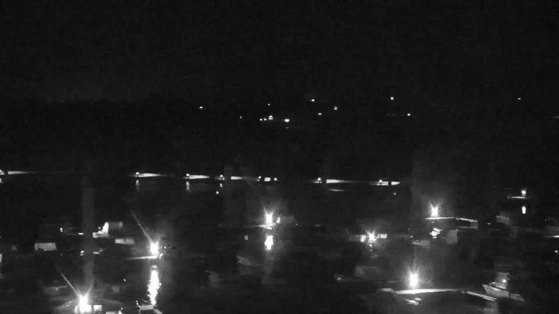 Numerous small lights illuminate a dark body of water at night, with a distant shoreline faintly visible in the background.