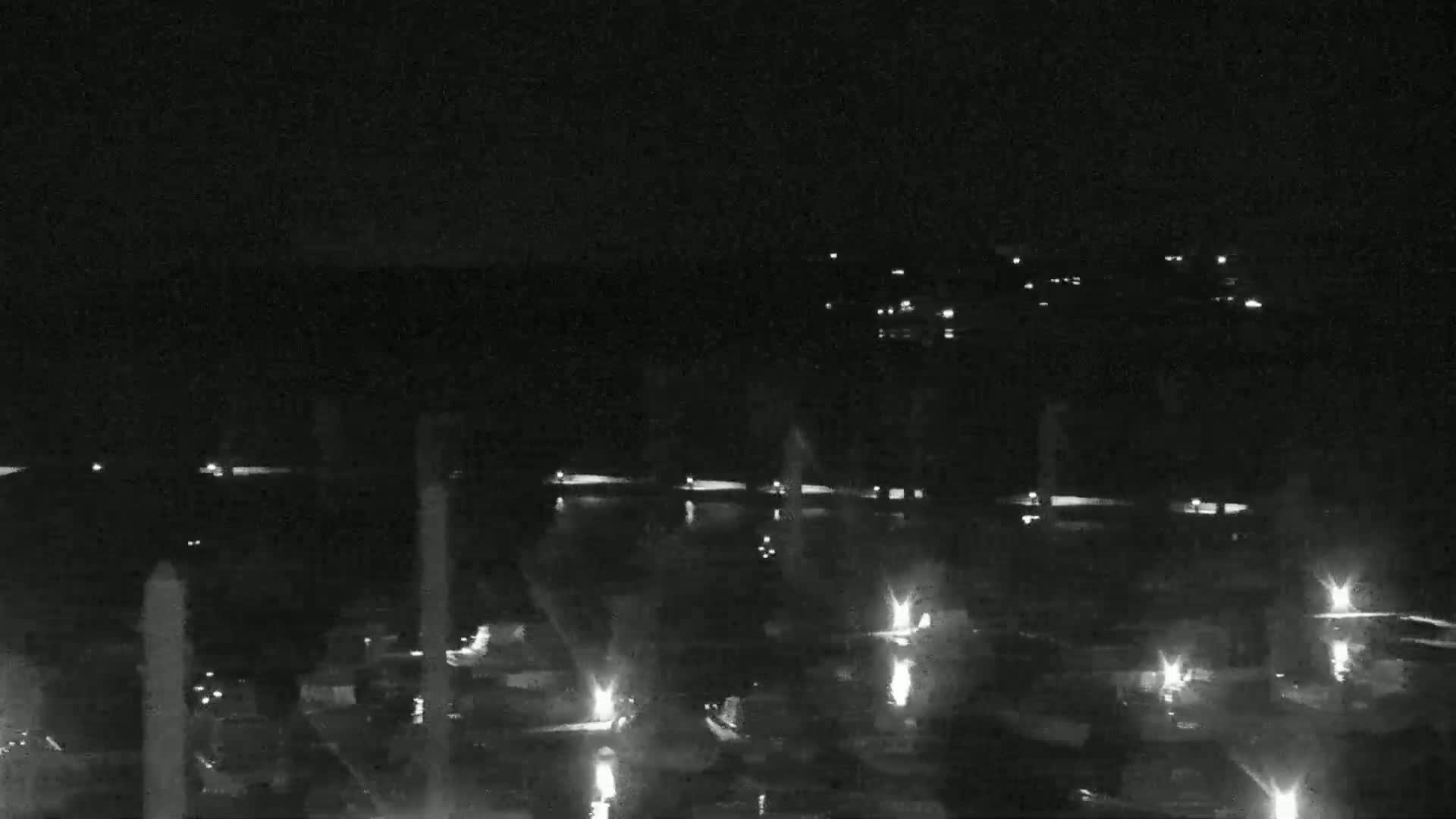 At night, numerous lights illuminate a dark body of water featuring several vertical fountains.