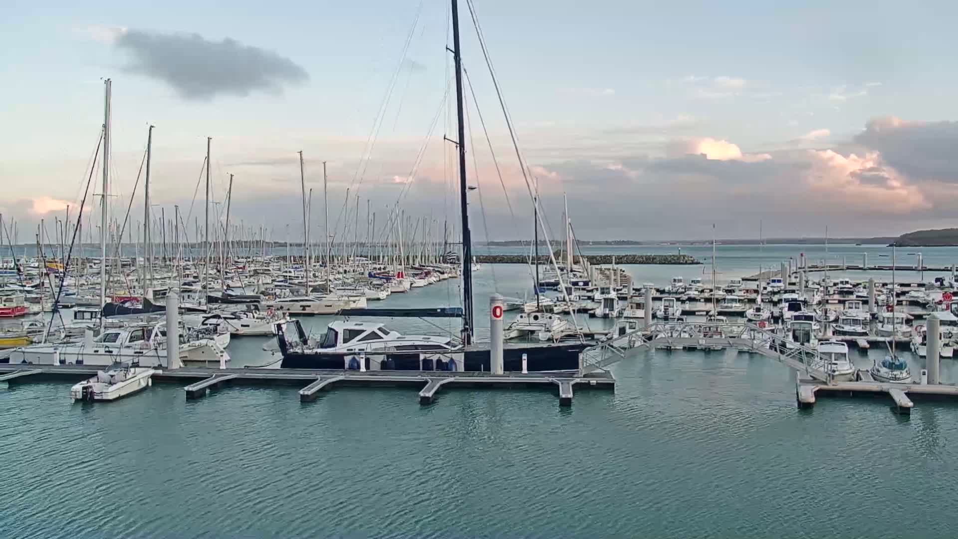 A marina filled with numerous sailboats and motorboats under a partly cloudy sky.