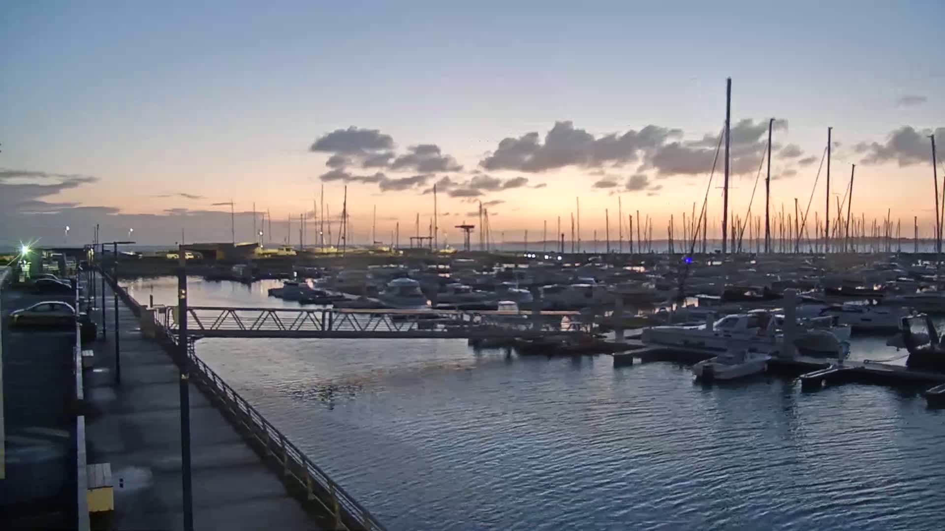 A marina filled with numerous sailboats and motorboats at sunset under a partly cloudy sky.
