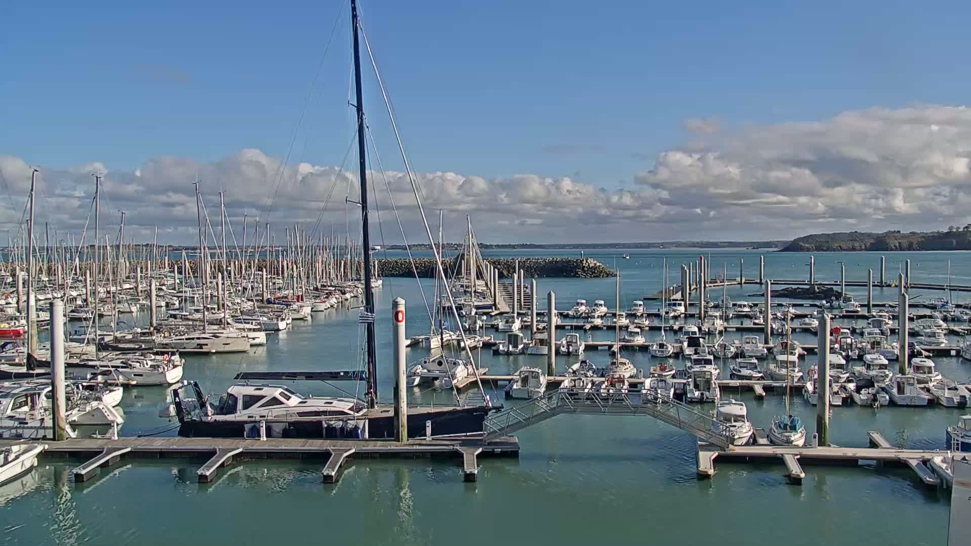 A marina filled with numerous sailboats and motorboats under a partly cloudy sky.