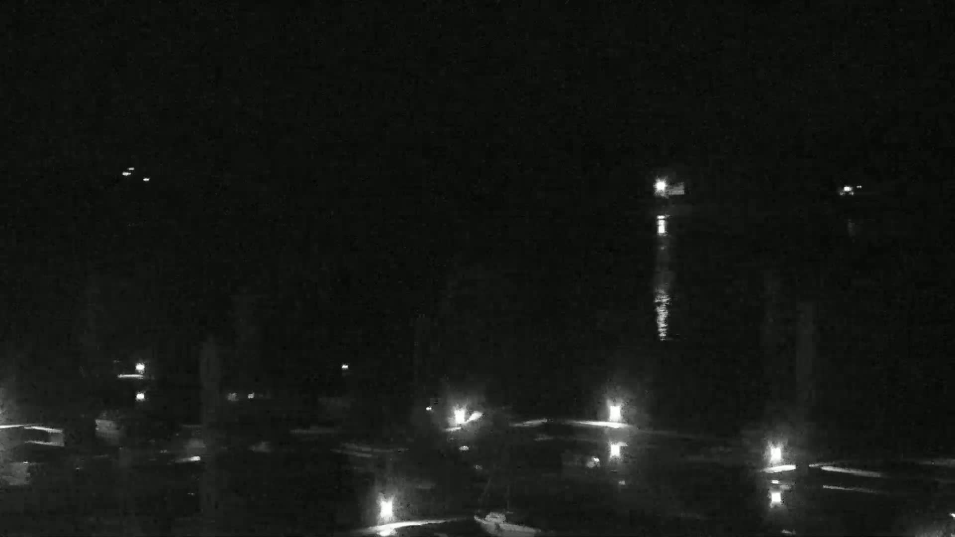 At night, a body of water reflects dim lights from a dock and several distant sources.