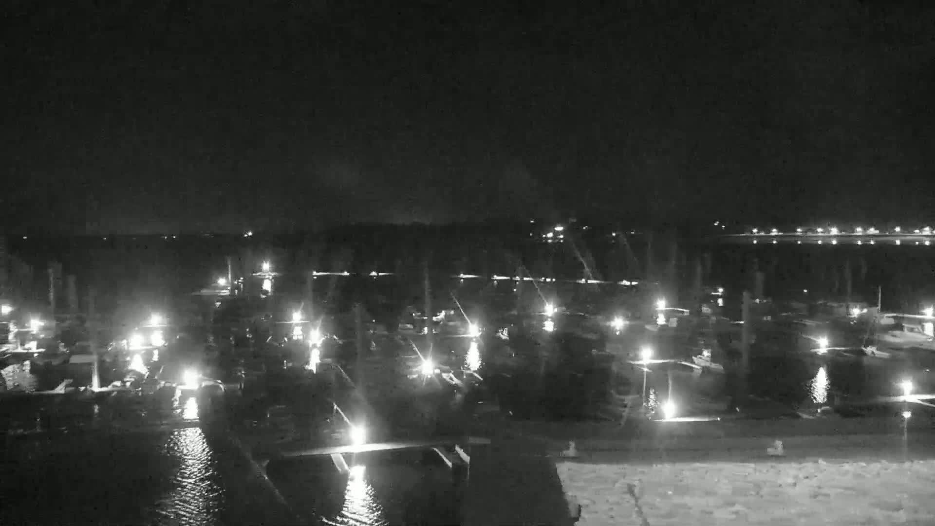 A nighttime, low-light view of a marina filled with numerous boats illuminated by lights, reflecting on the calm water.
