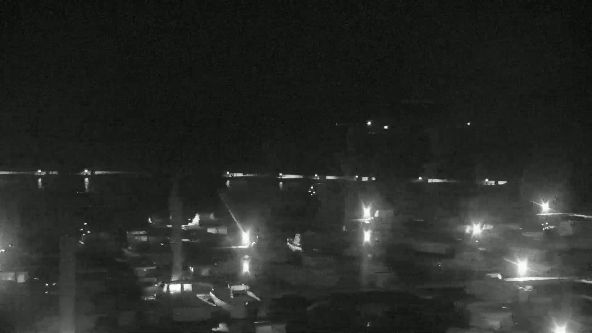 At night, many small lights illuminate a dark body of water with boats moored along its edge.