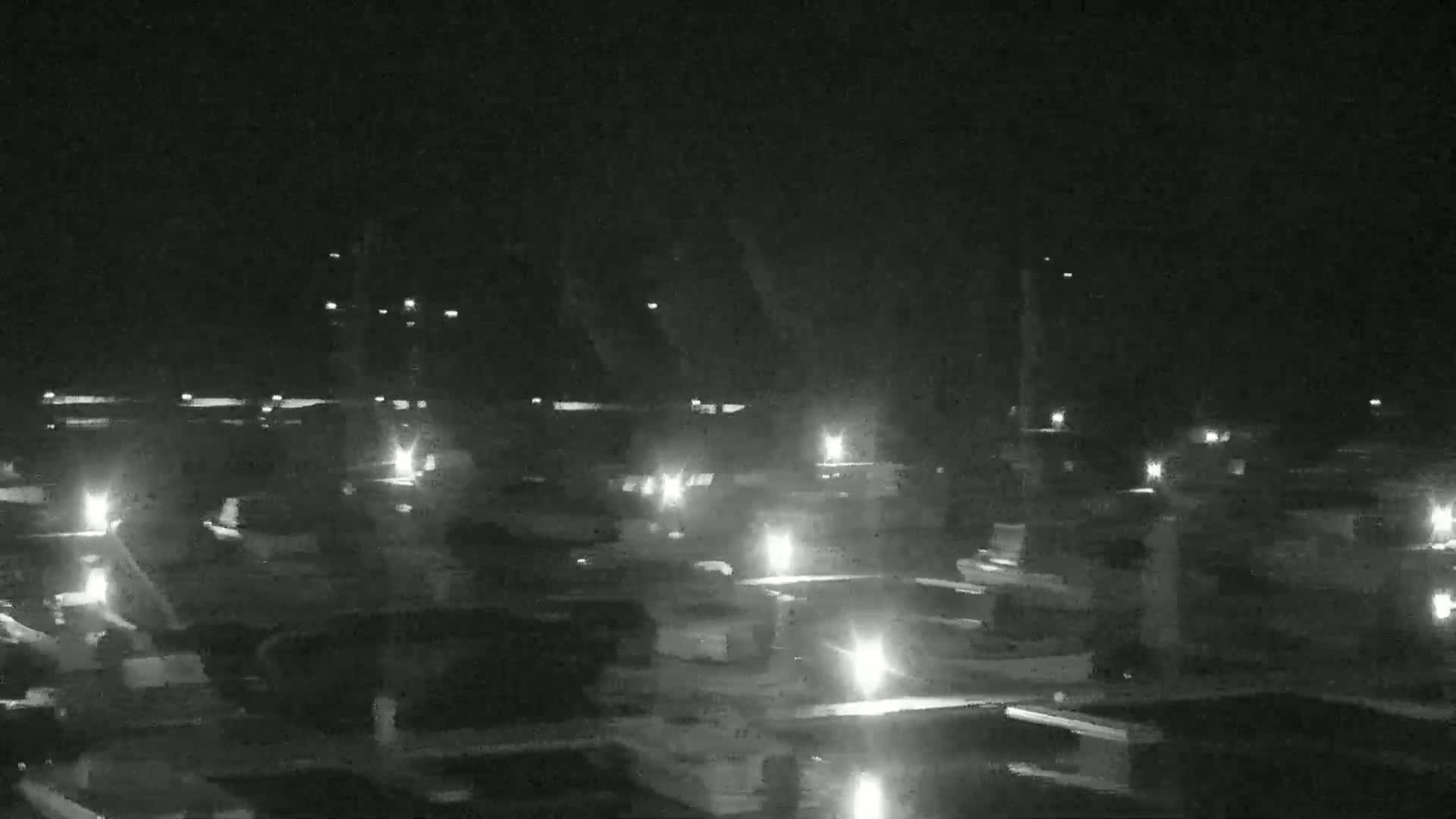 A nighttime aerial view shows numerous boats in a marina, illuminated by scattered lights.