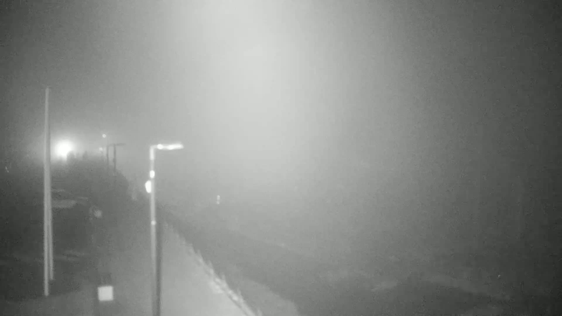 A foggy night scene shows a path or road with lampposts, extending into a dense fog.