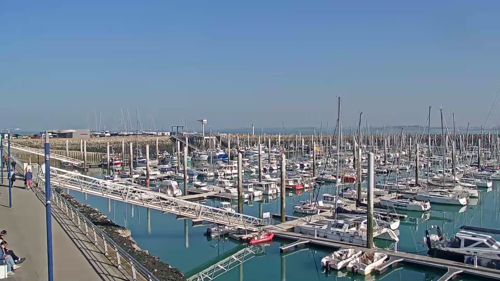 A marina filled with numerous boats and yachts is shown on a sunny day.