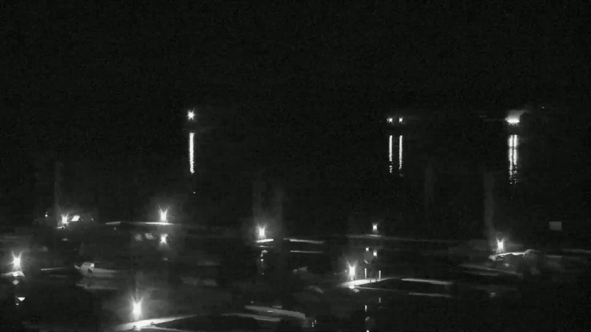 A nighttime view of a calm body of water reflecting lights from buildings and streetlights on the shore.