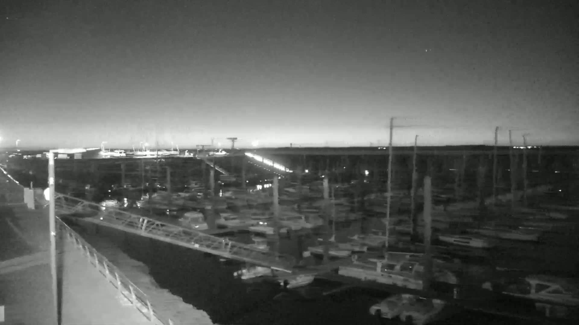 A nighttime, grayscale image shows a marina filled with numerous boats under a mostly clear sky.
