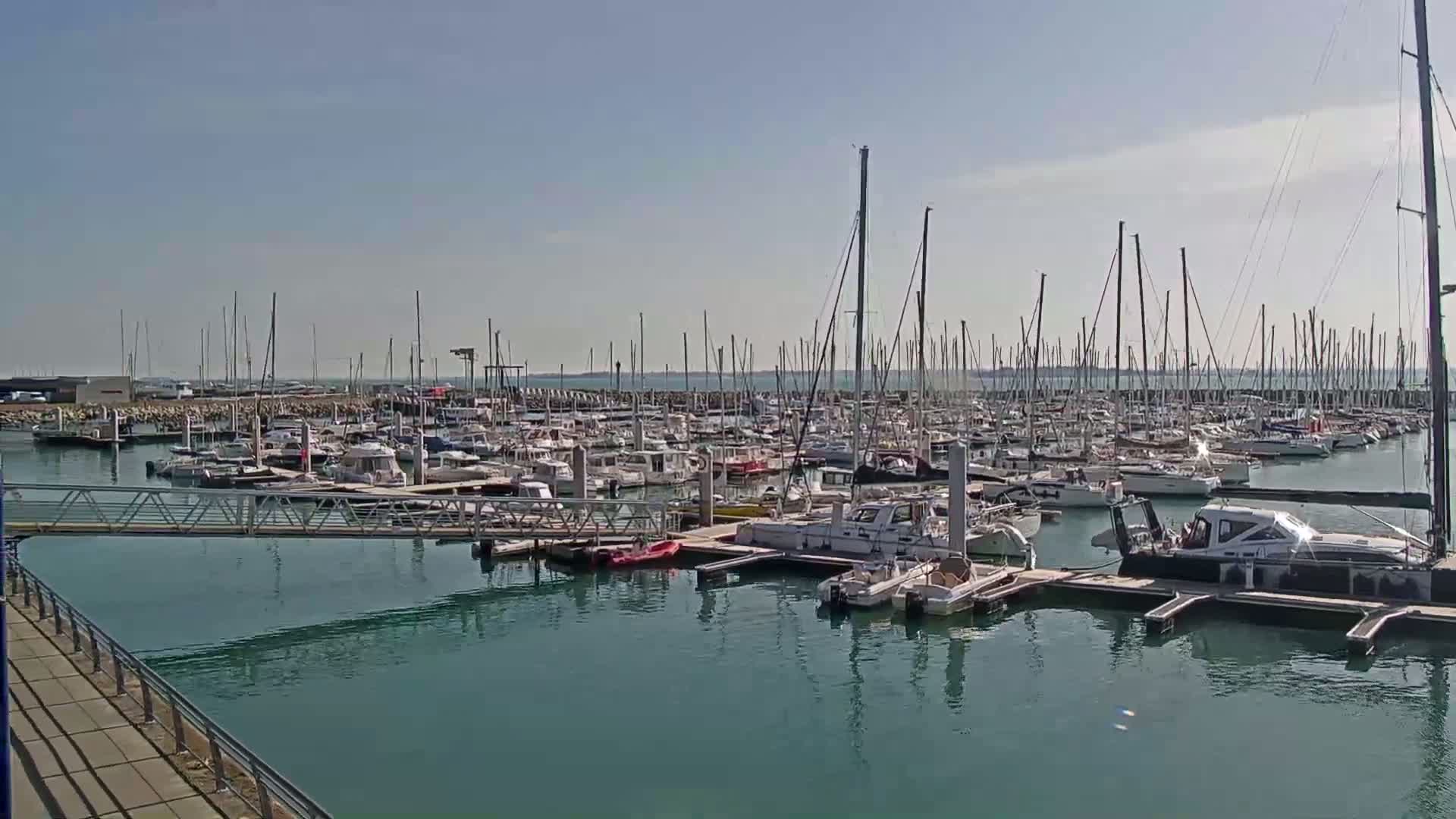 A marina filled with numerous sailboats and motorboats is shown on a sunny day.
