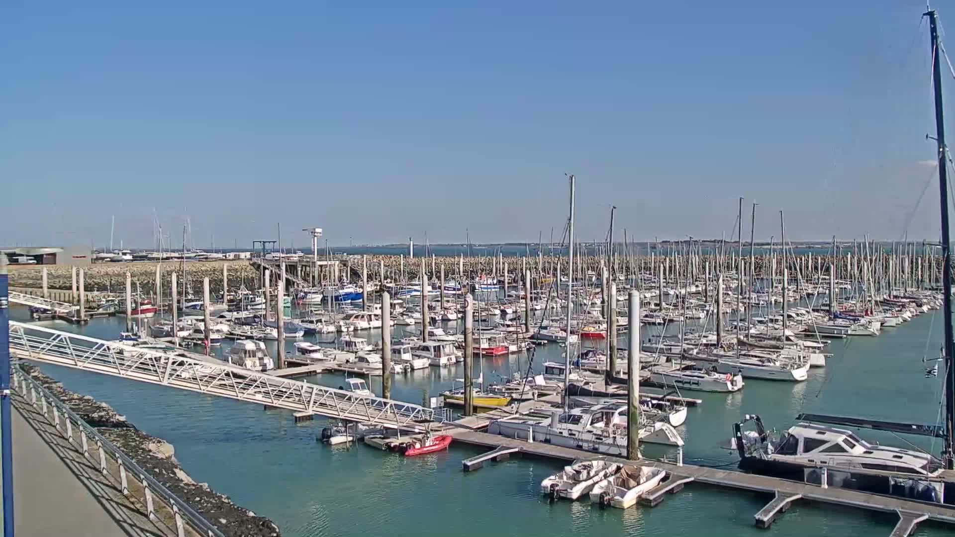 A large marina filled with numerous sailboats and motorboats on a sunny day.