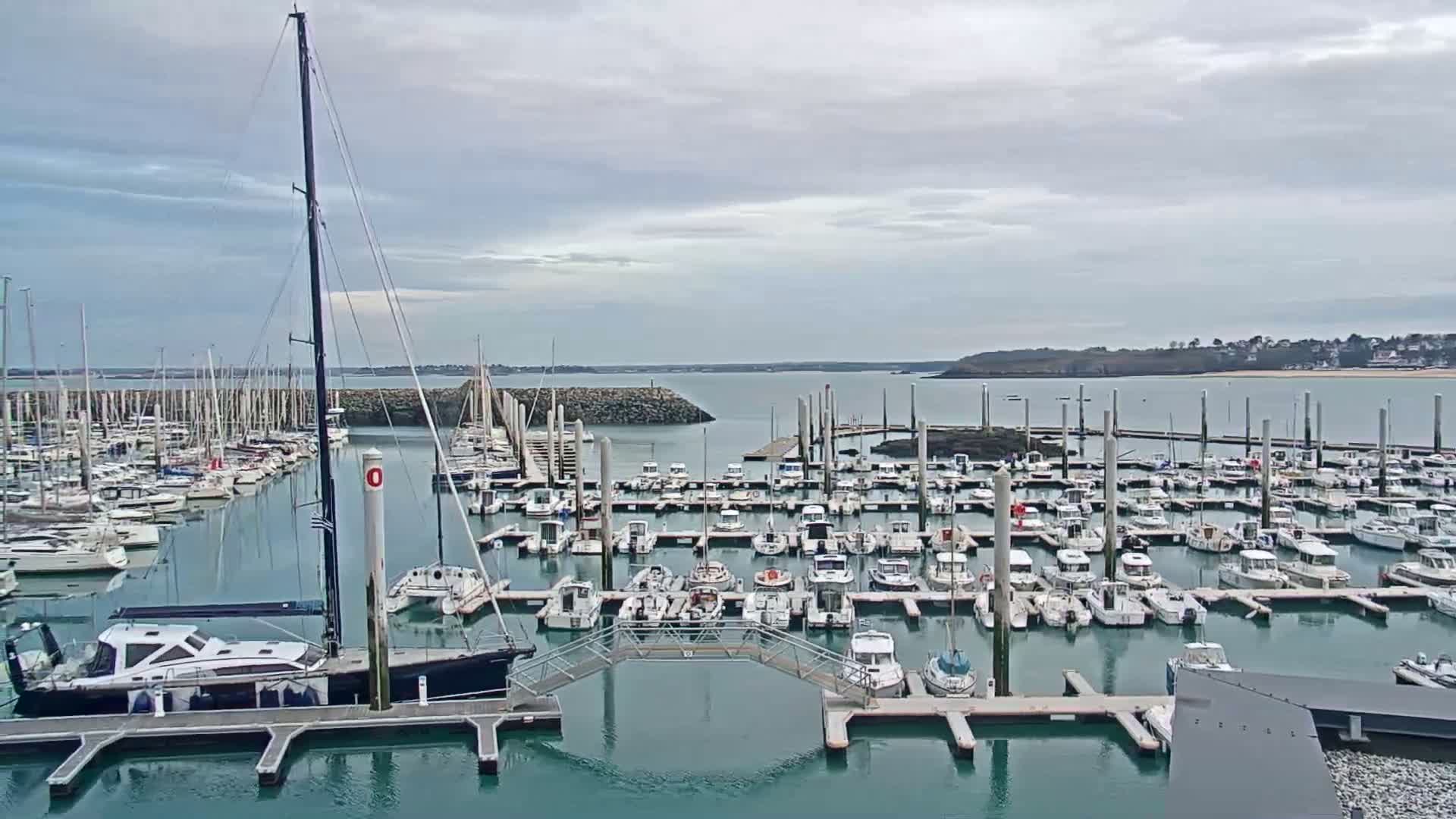A marina filled with numerous sailboats and motorboats is shown under a cloudy sky.