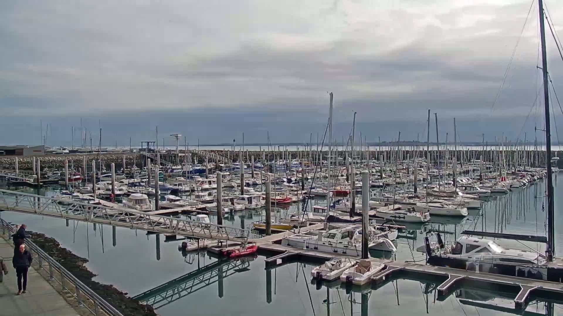 A marina filled with numerous sailboats and motorboats under a cloudy sky.