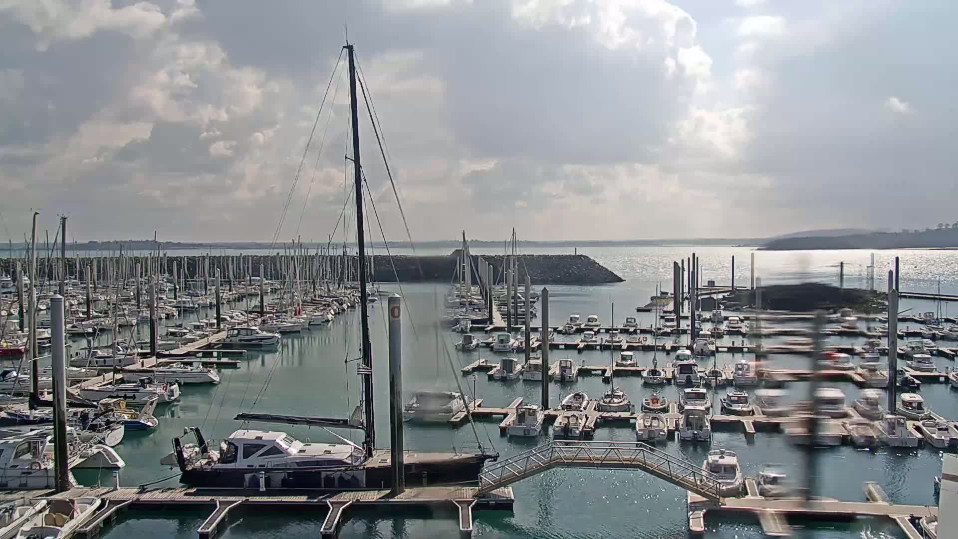 A marina filled with numerous sailboats and motorboats is seen under a partly cloudy sky.