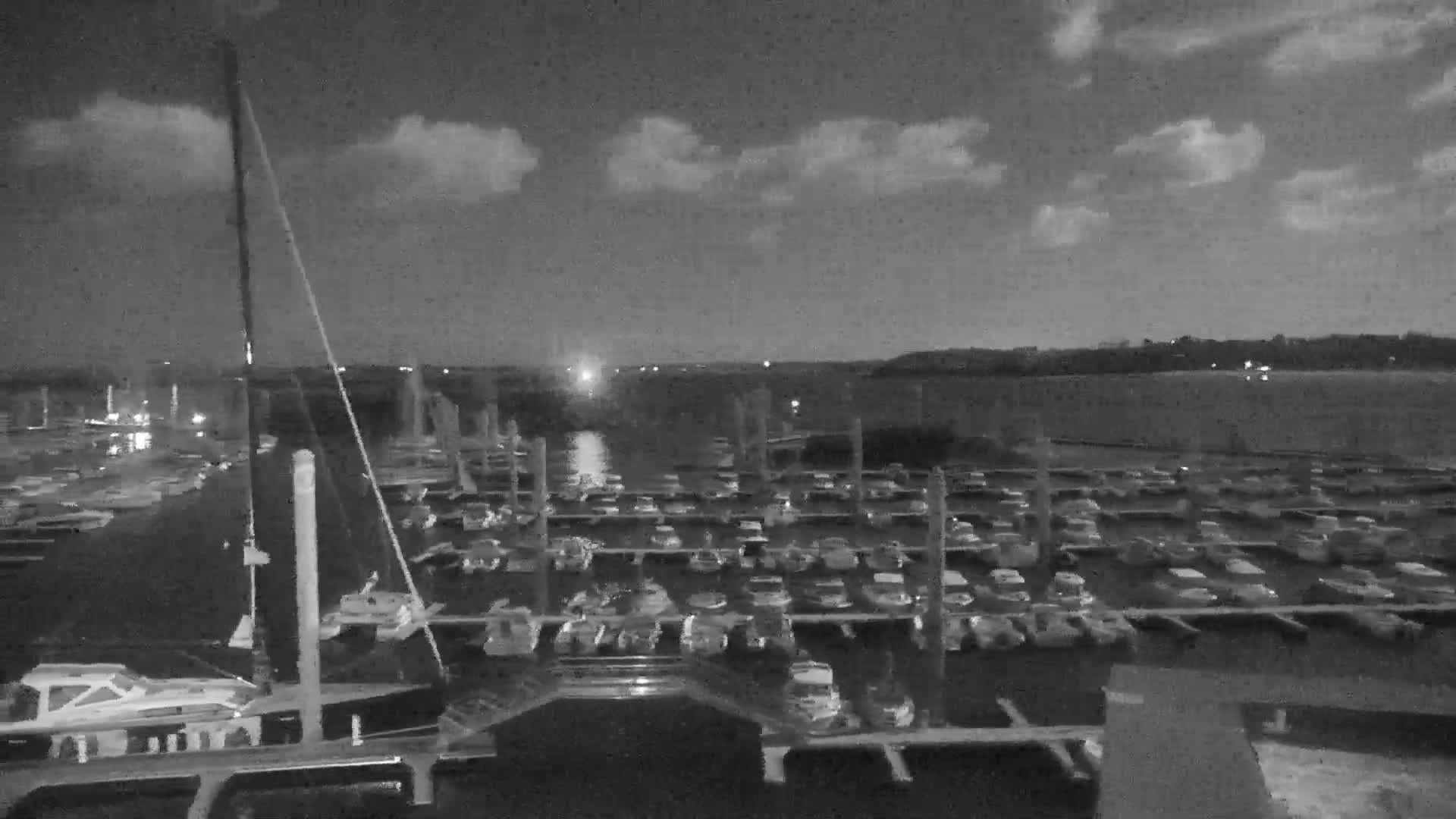 A nighttime view of a marina filled with numerous boats under a partly cloudy sky.
