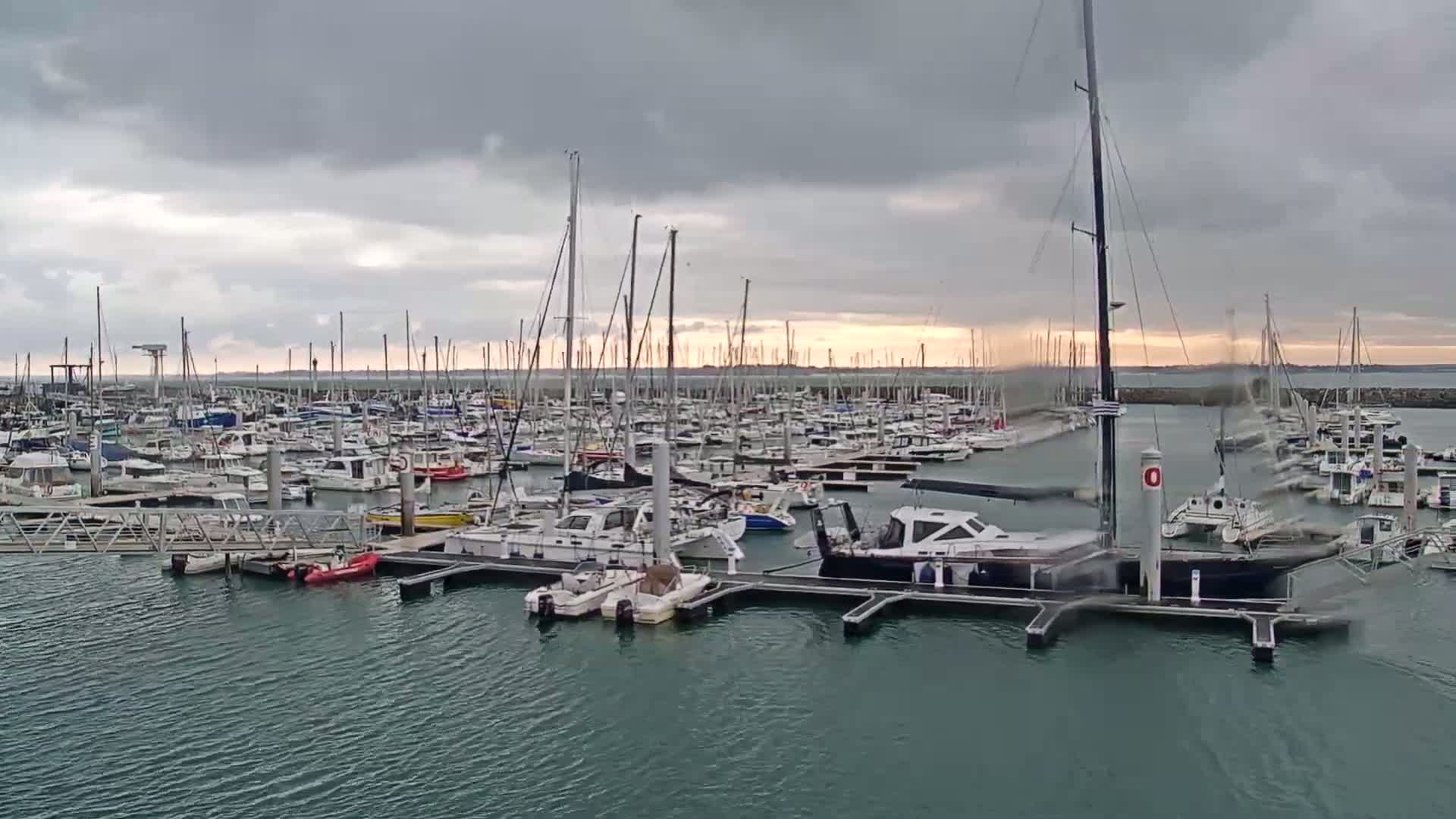 A marina filled with numerous sailboats and motorboats under a cloudy sky.
