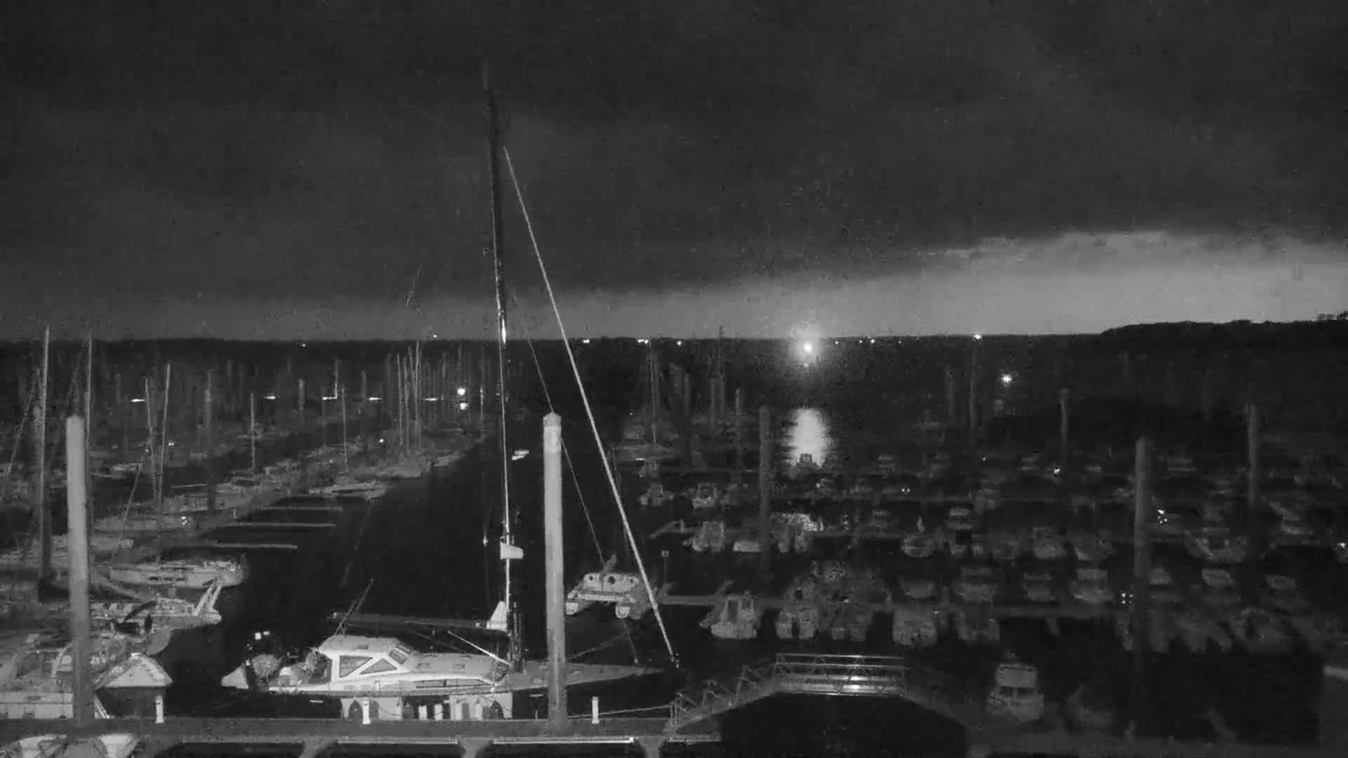 A nighttime view of a marina filled with numerous boats under a dark, cloudy sky.